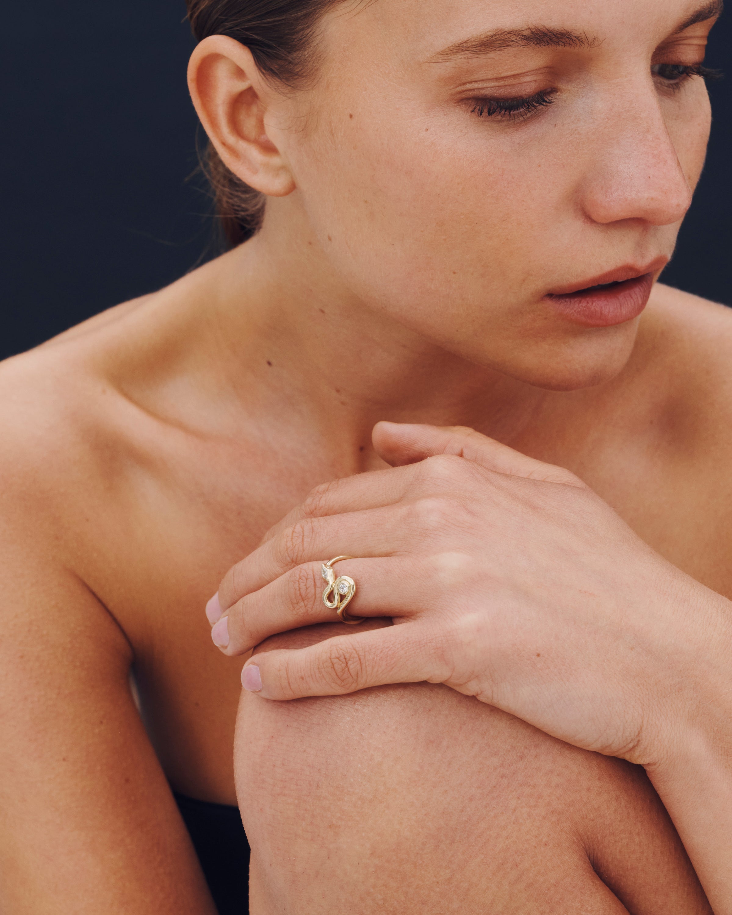 Woman with a gold ring on her finger, holding her shoulder against a dark background