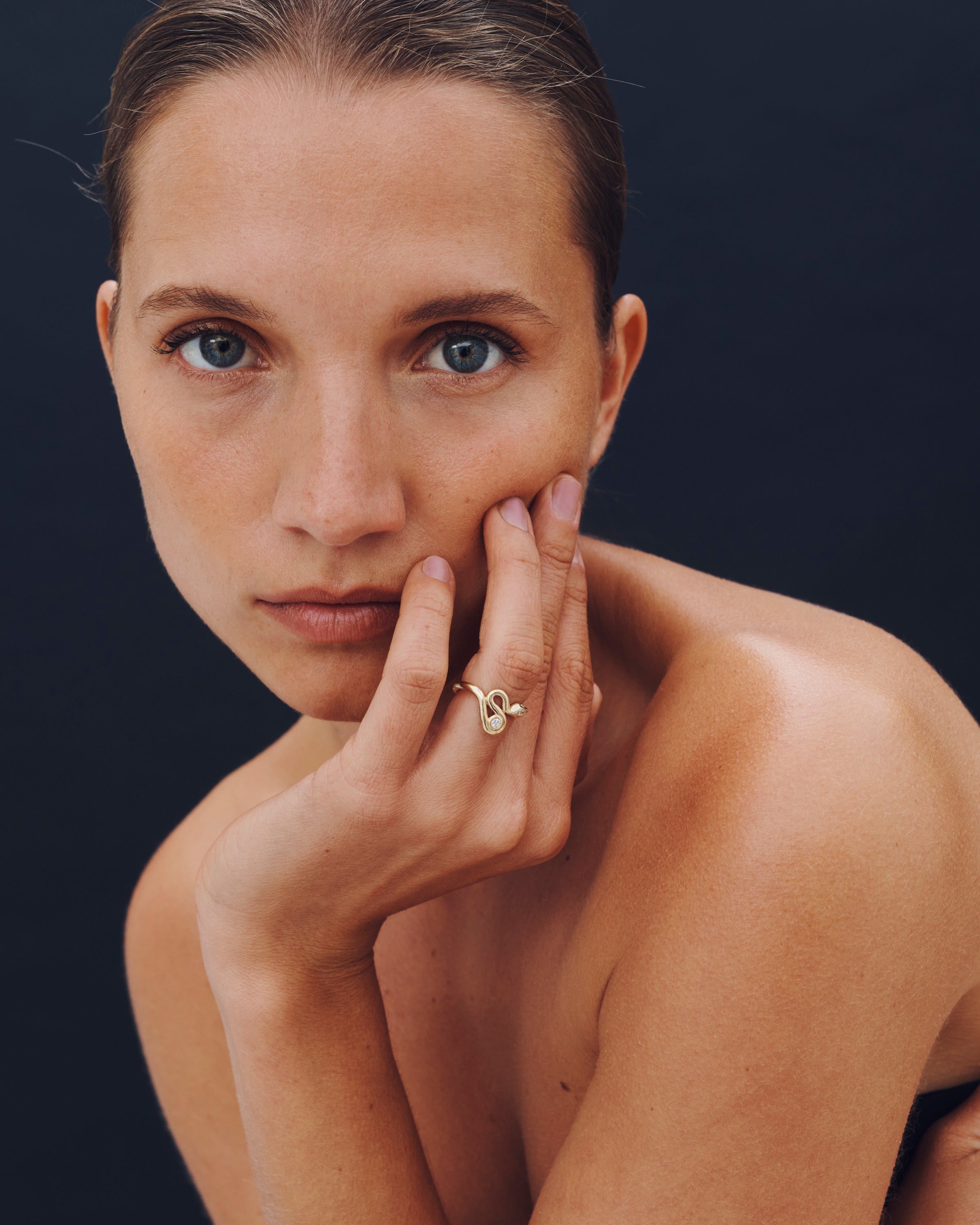 Woman with a gold ring on her finger against a dark background