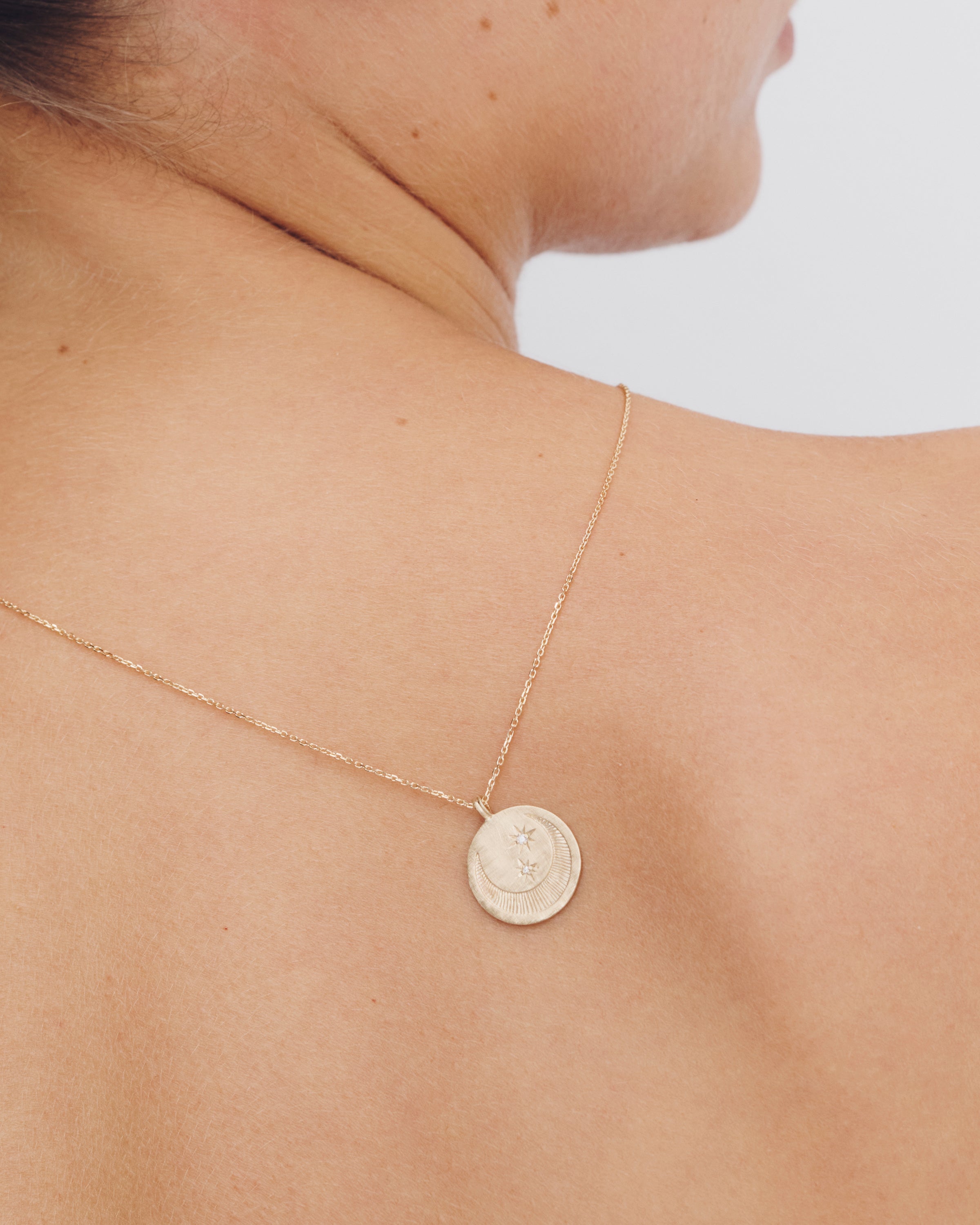 Gold necklace with a round pendant on a person's neck against a neutral background