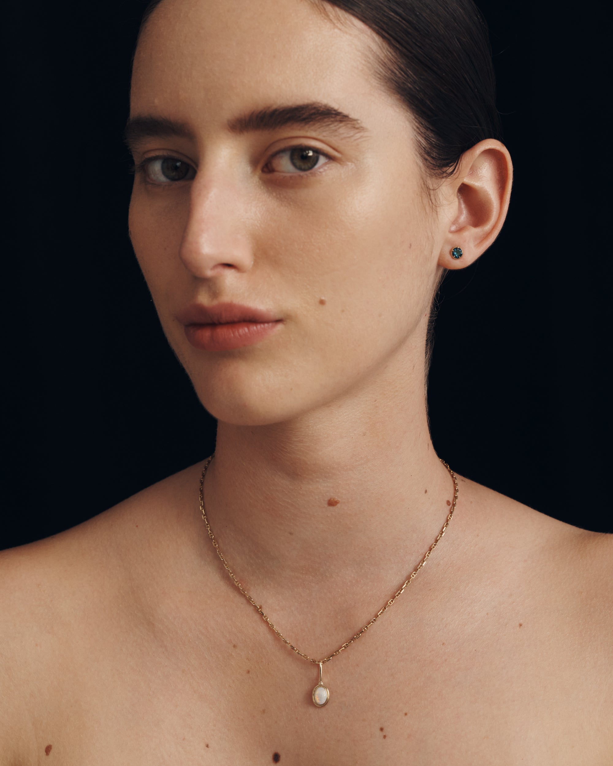 Woman wearing a delicate necklace against a black background