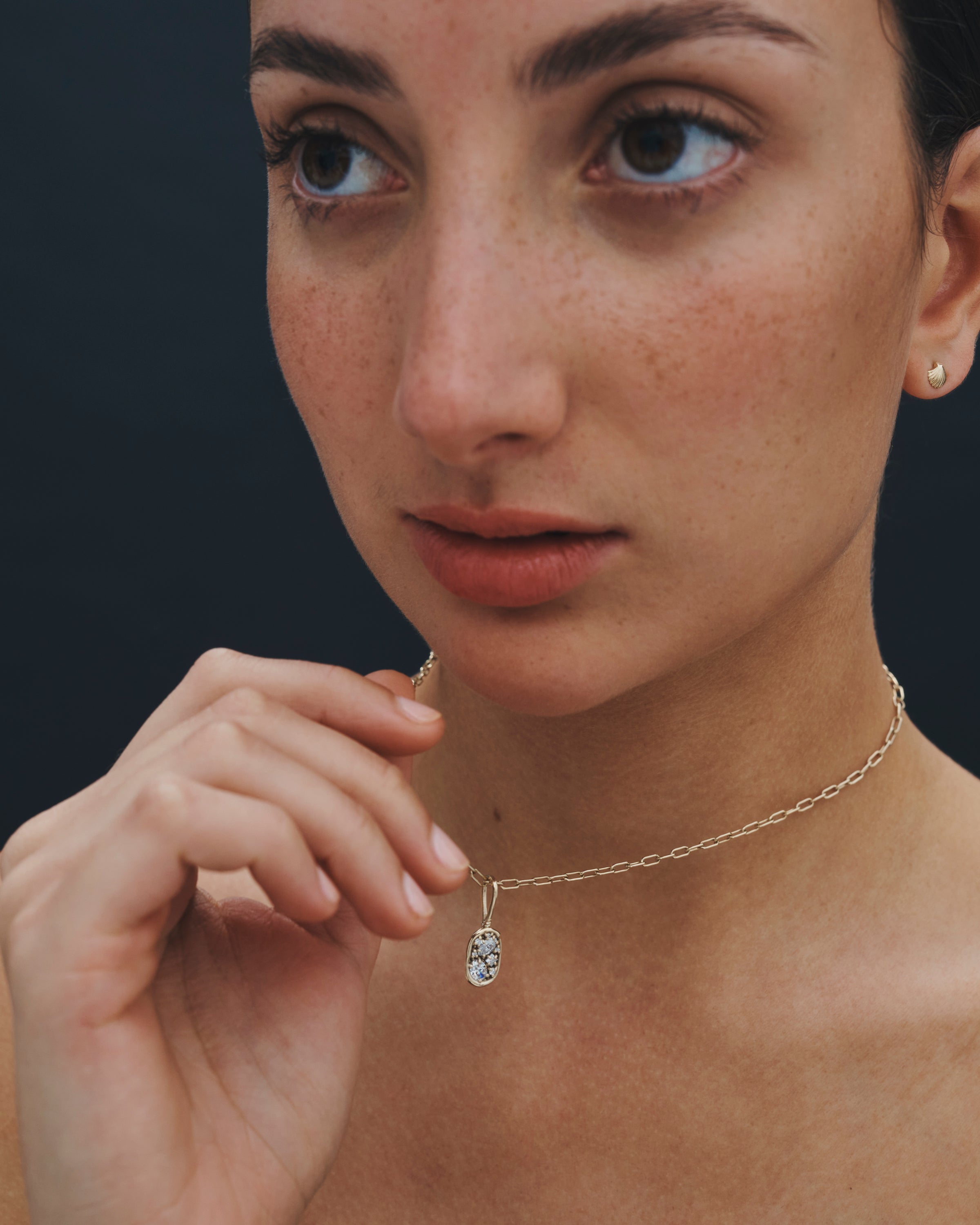 Close-up of a woman wearing a gold necklace with a pendant against a dark background