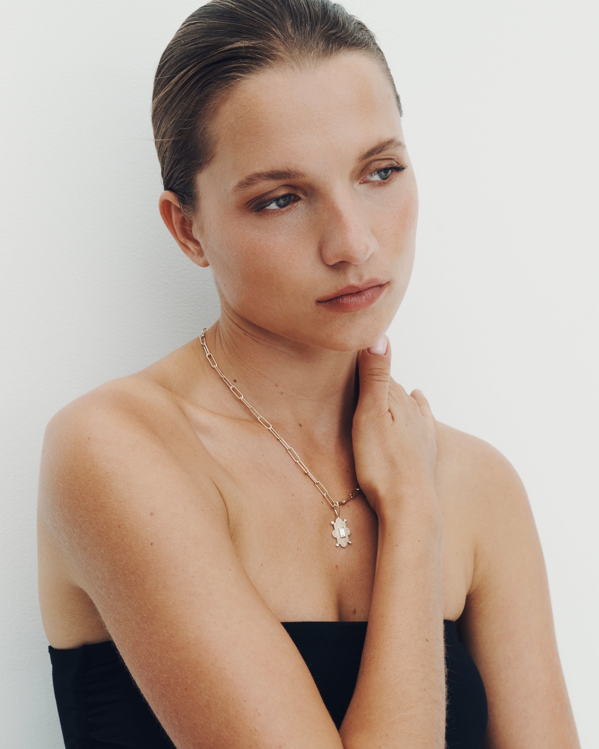Woman wearing a gold necklace with a clear pendant on a plain background