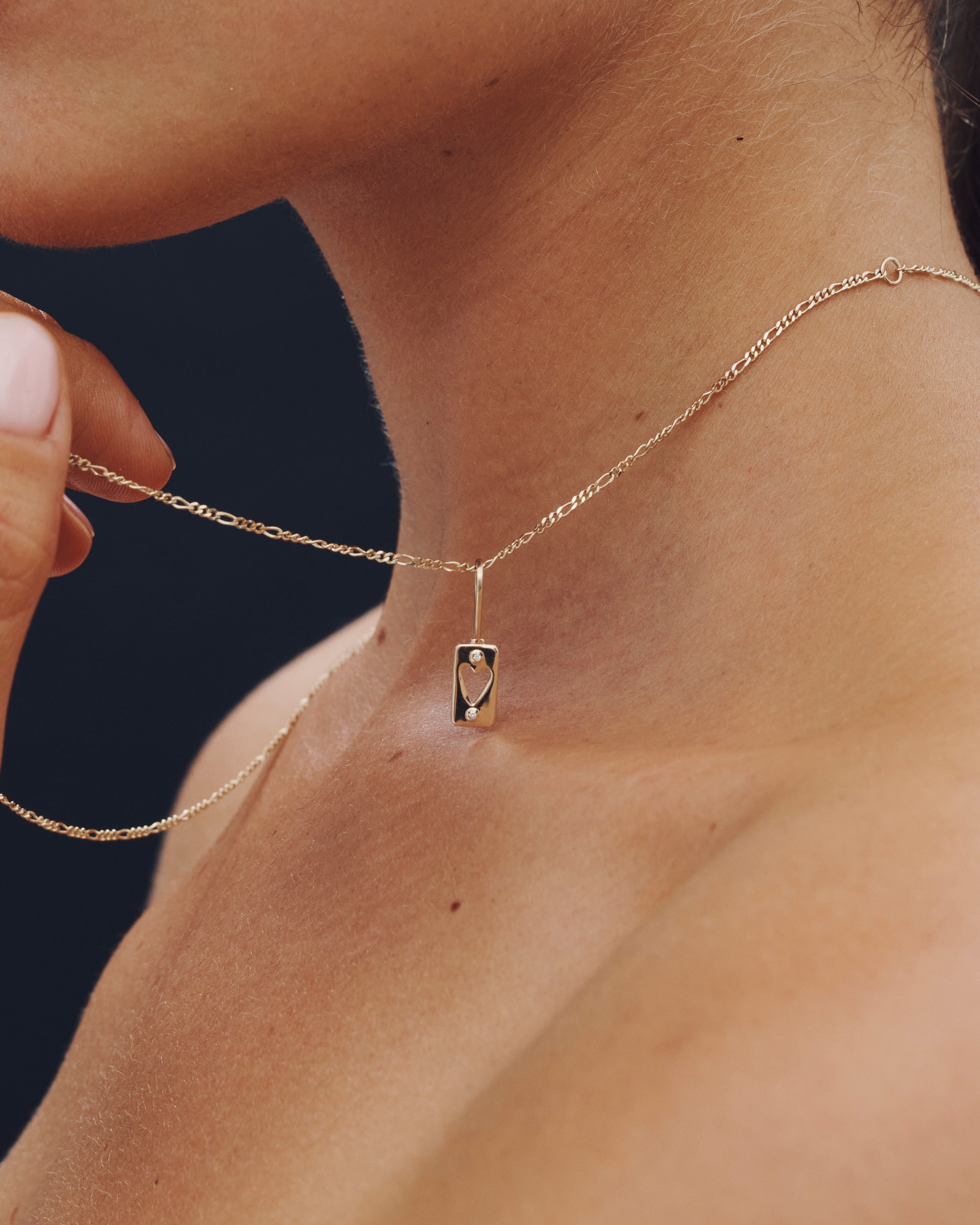 Gold necklace with a pendant on a person's neck against a dark background