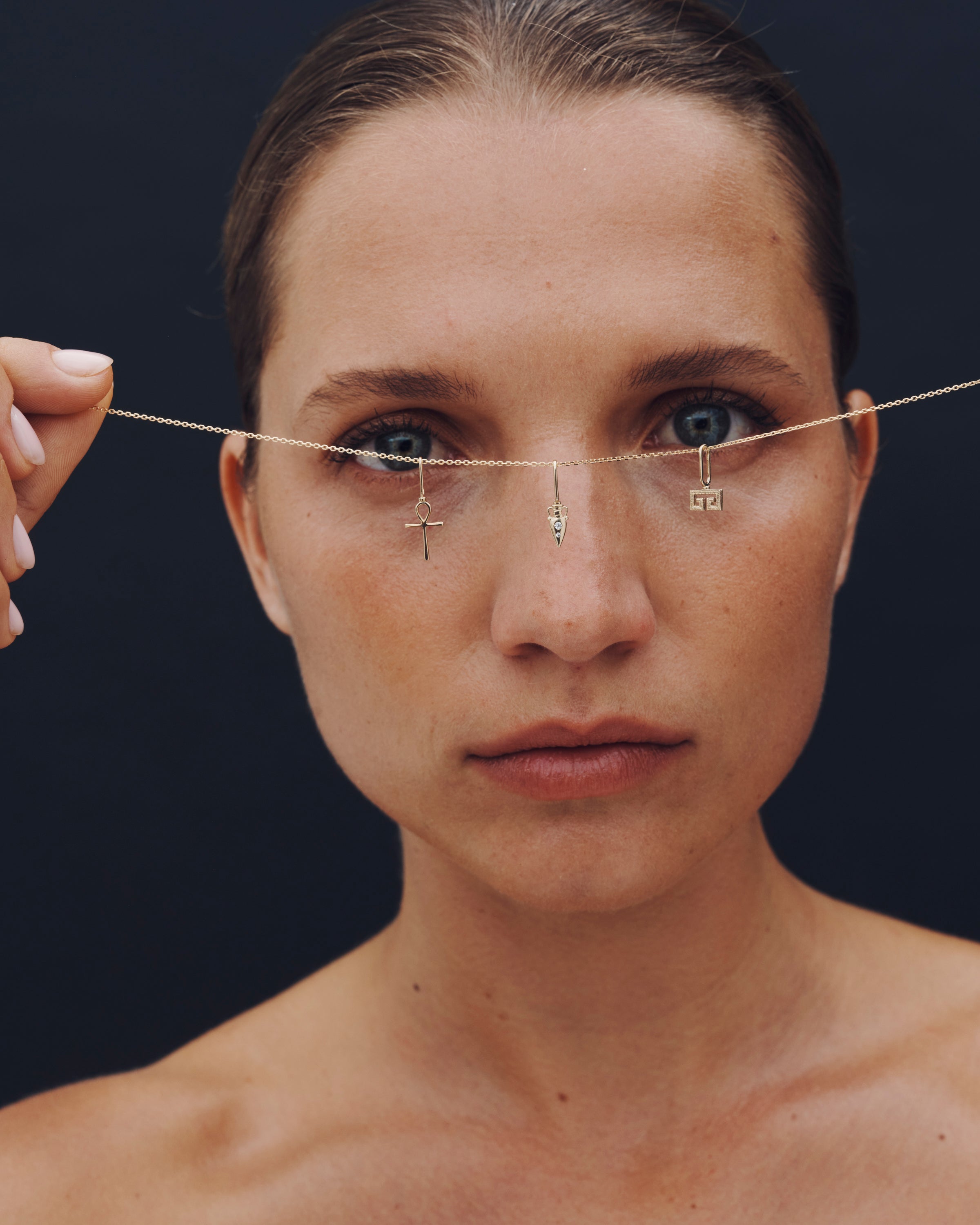 Woman with a thin gold chain with small pendants around her face against a dark background