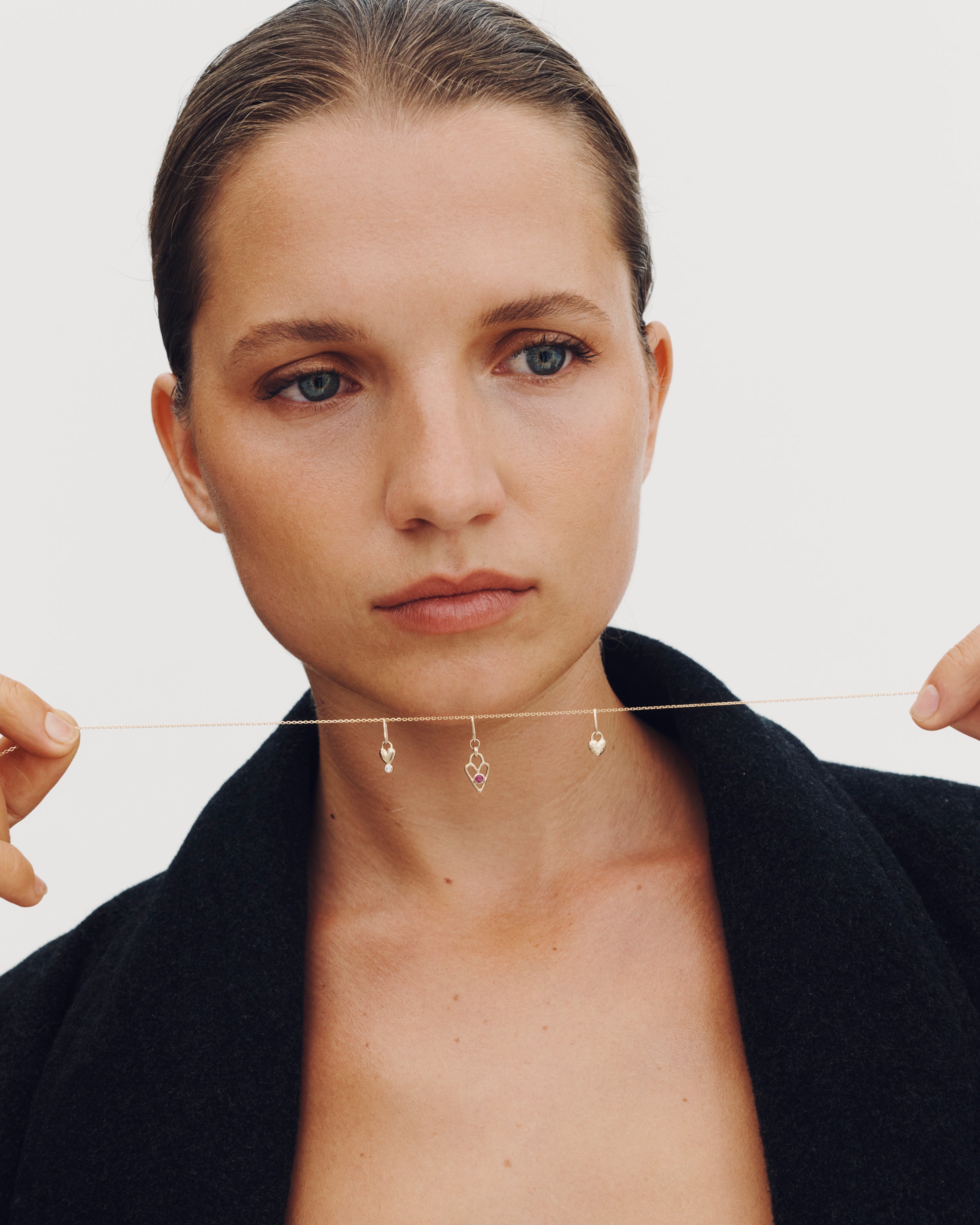 Woman balancing a thin rod on her face with earrings on a plain background