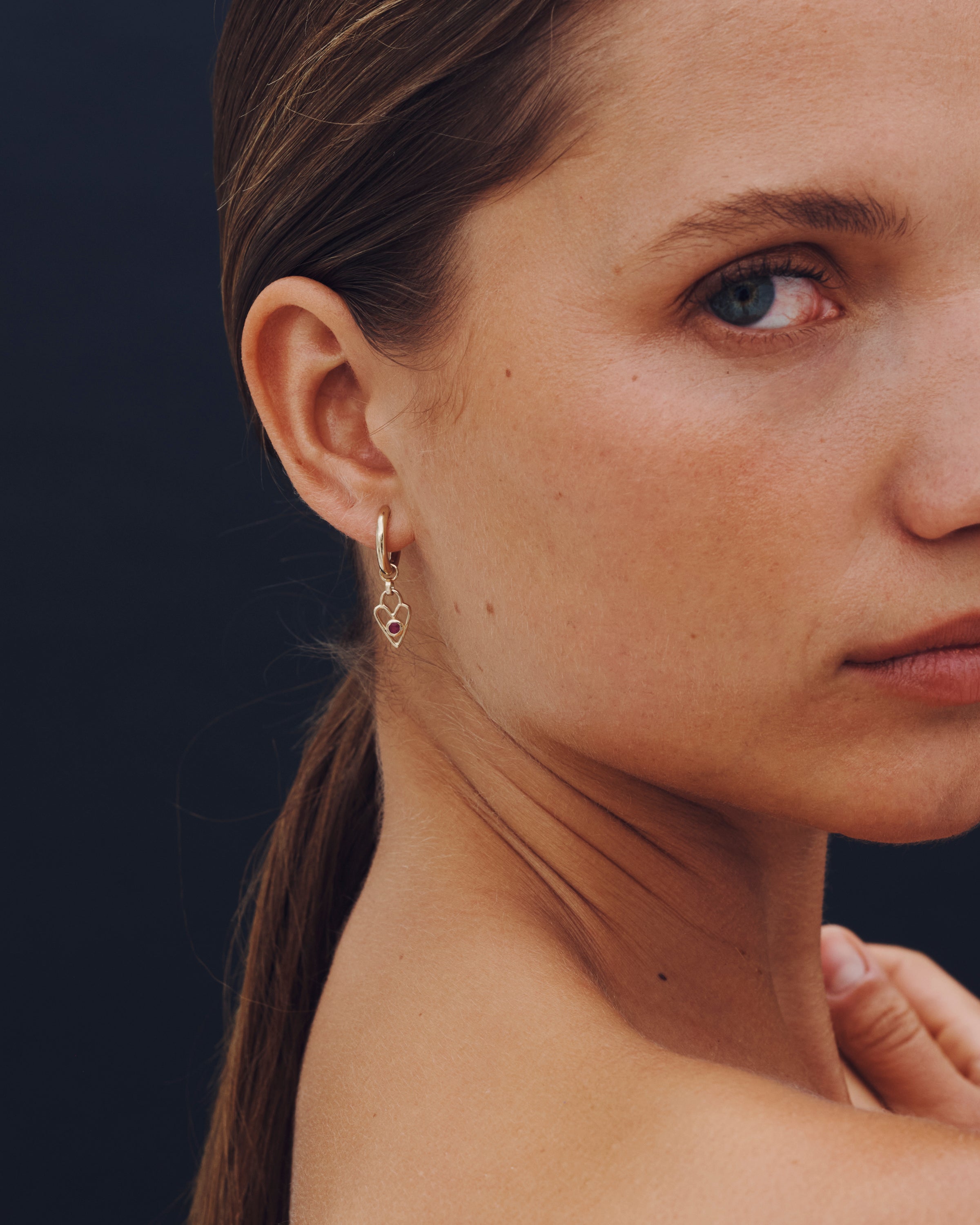 Close-up of a woman wearing gold hoop earrings with a dark background