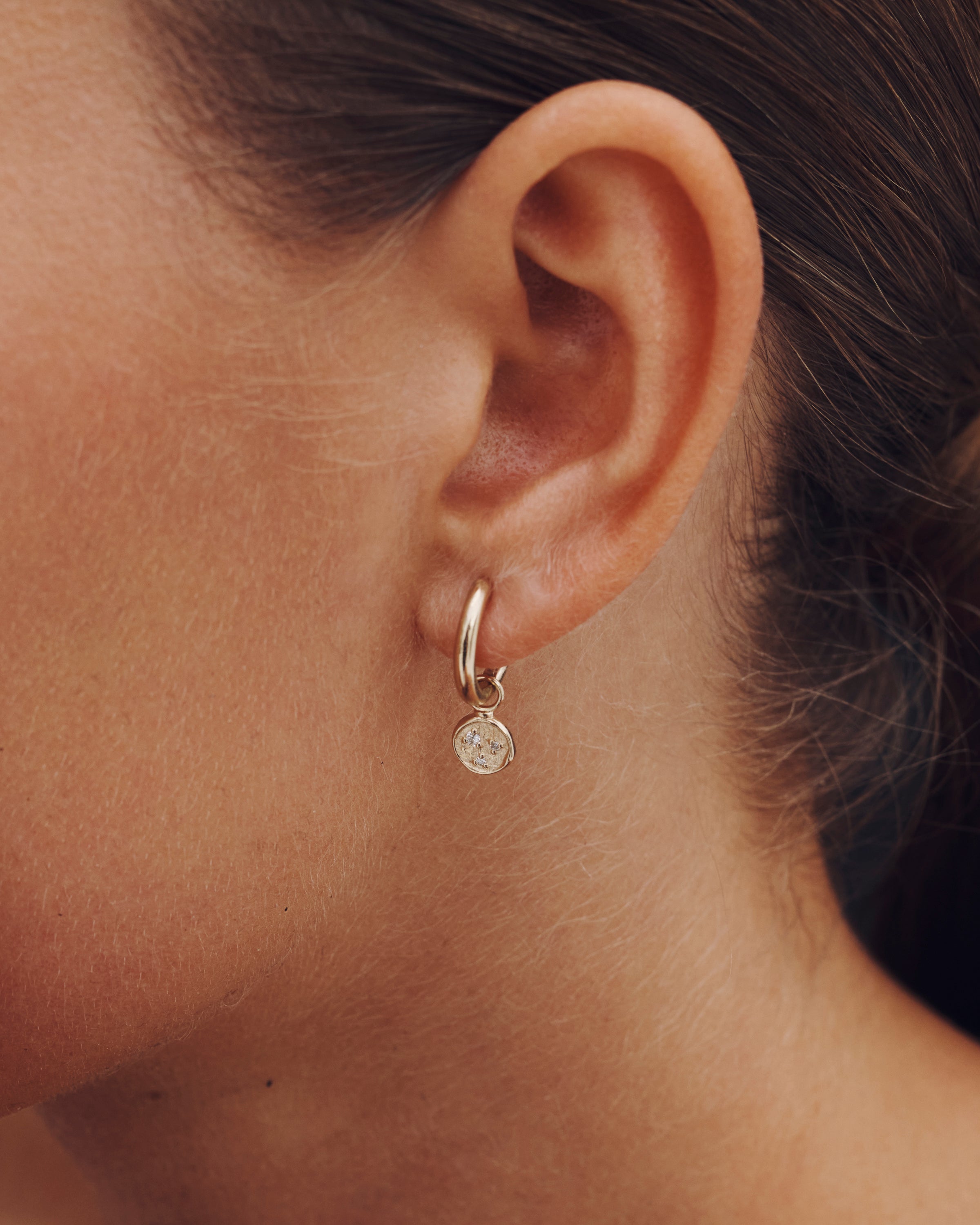 Close-up of an ear wearing a small hoop earring with a round gemstone.