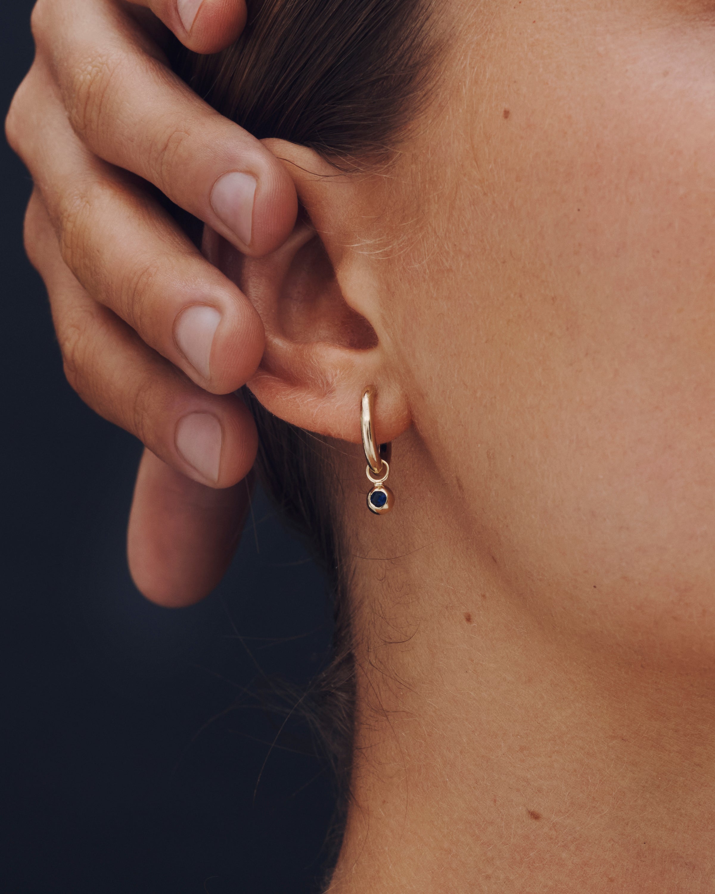 Close-up of a person wearing a gold hoop earring with a small gemstone.