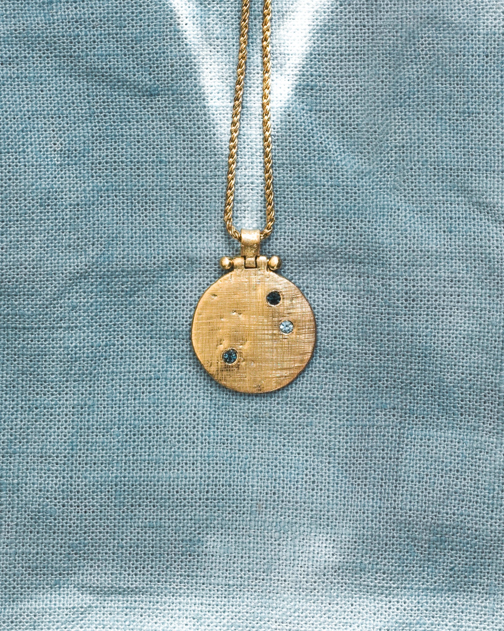 Gold necklace with a round pendant on a textured blue background