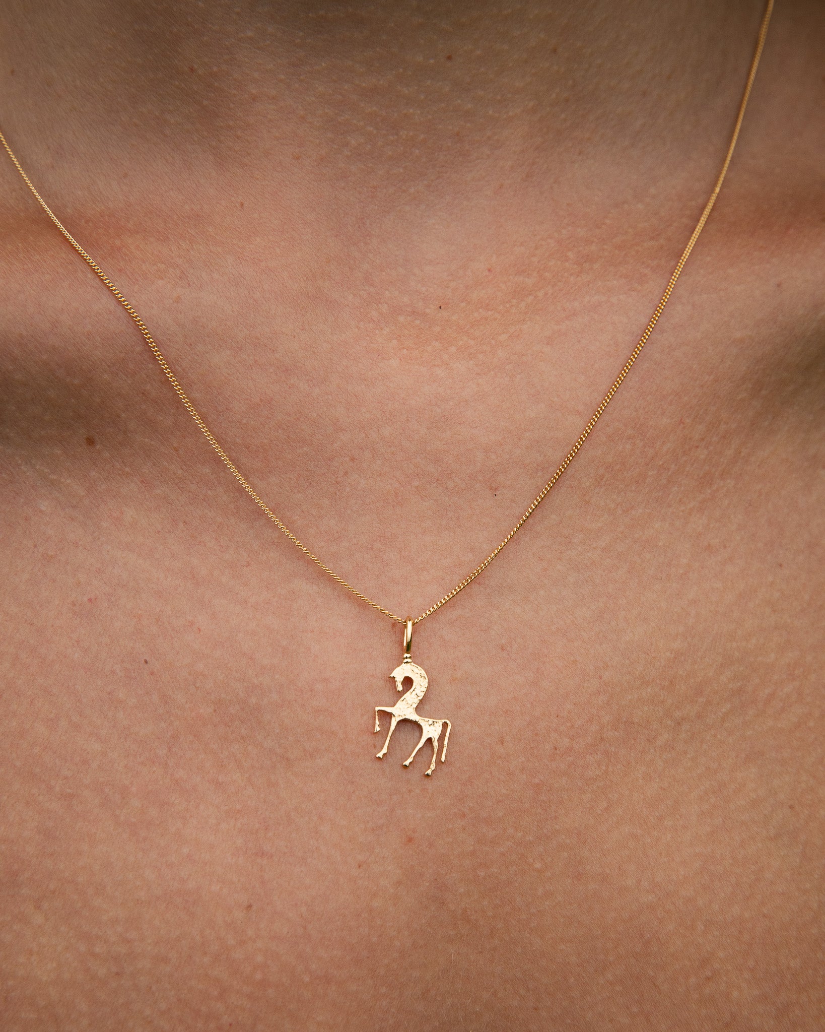 Gold necklace with a unicorn pendant on a person's neck