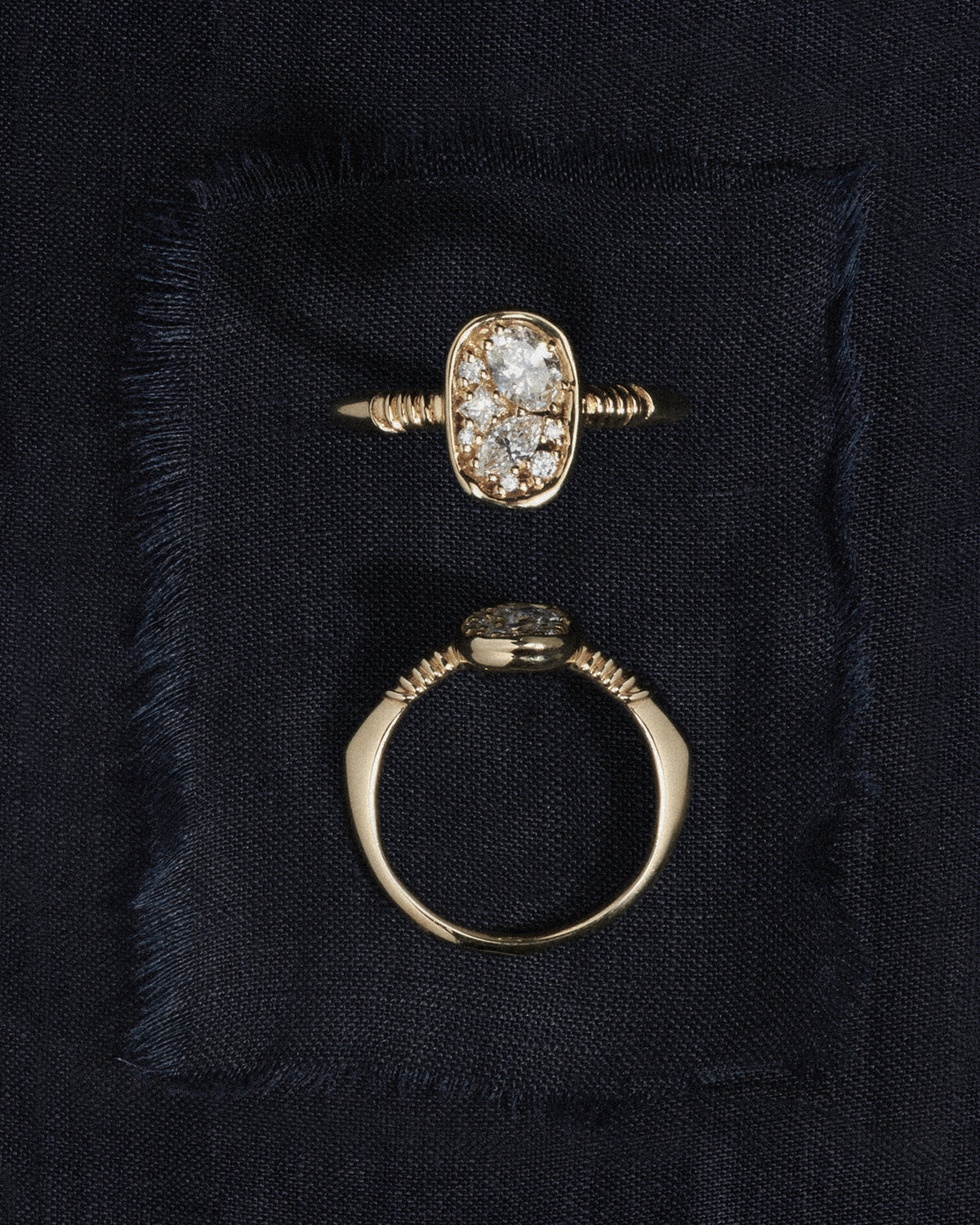 Two gold rings with diamond-like stones on a black fabric background