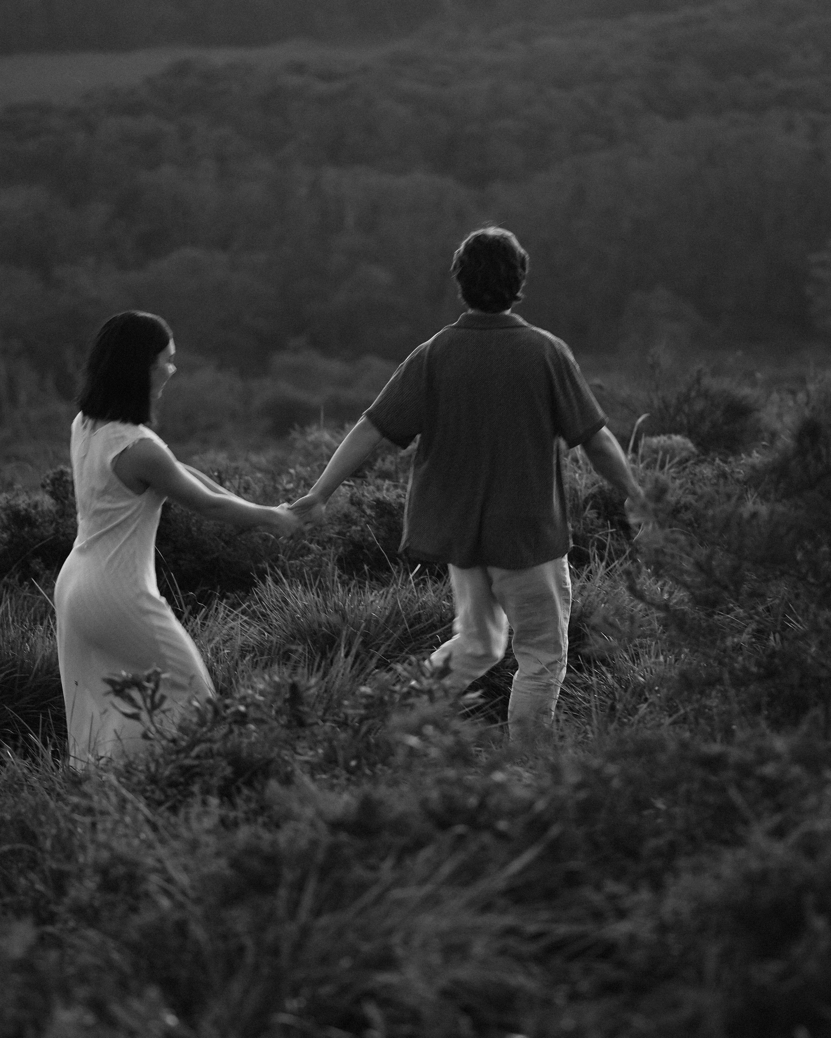 Two people walking hand in hand through a grassy field.