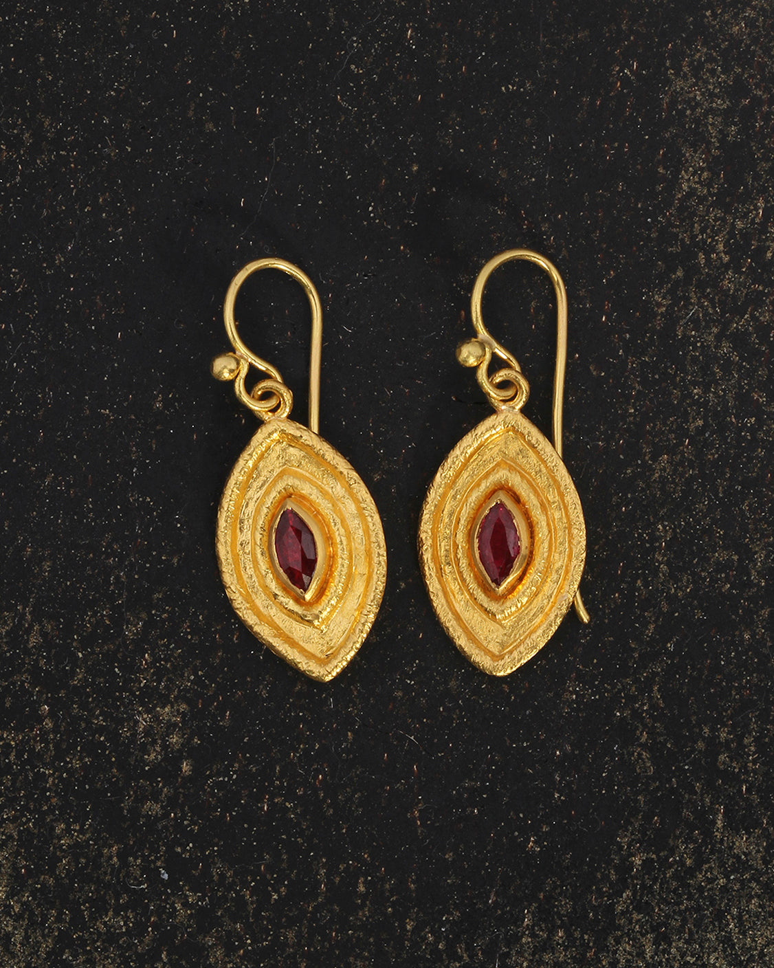 Gold earrings with red gemstones on a dark background