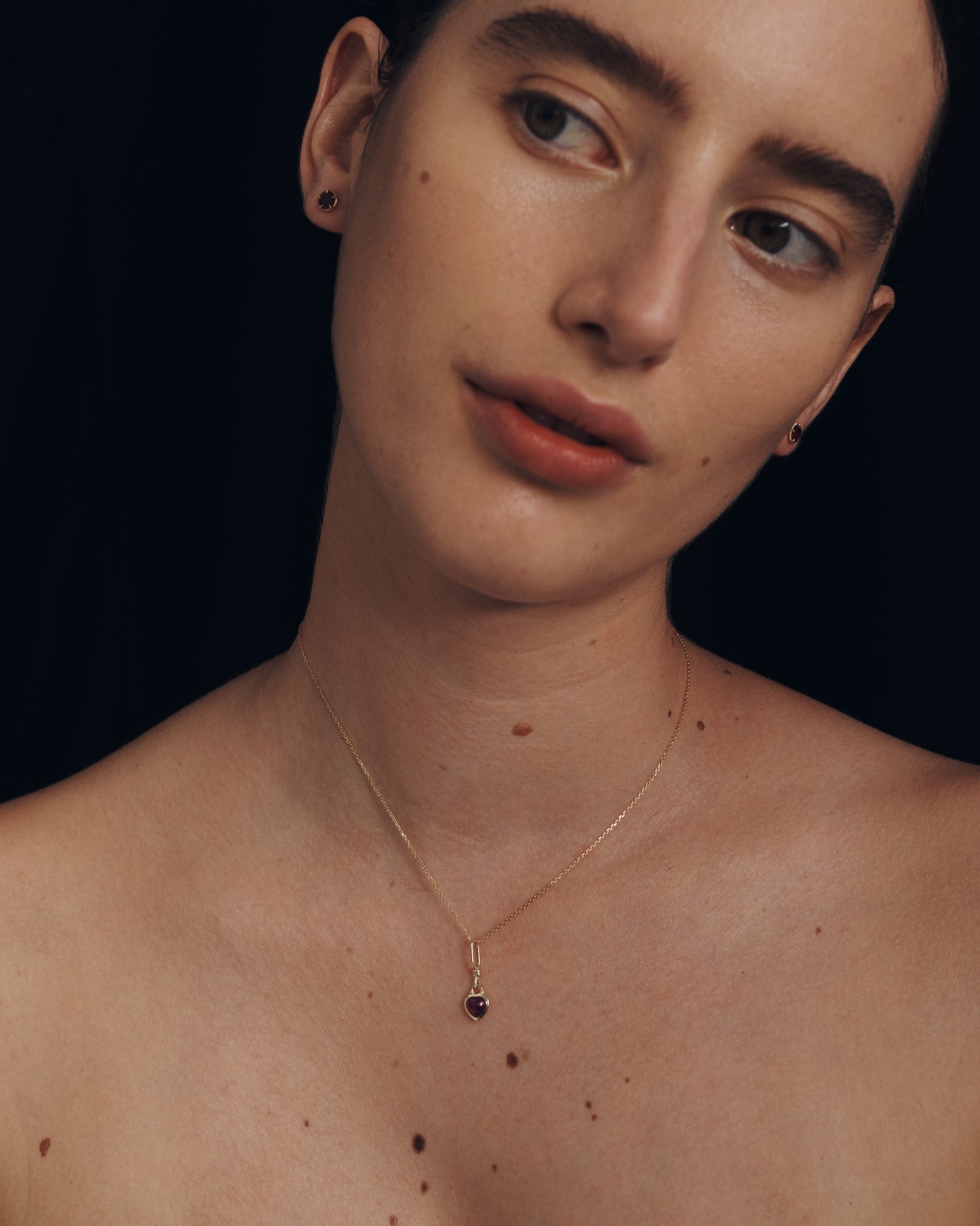 Person wearing a gold necklace with a dark pendant against a black background