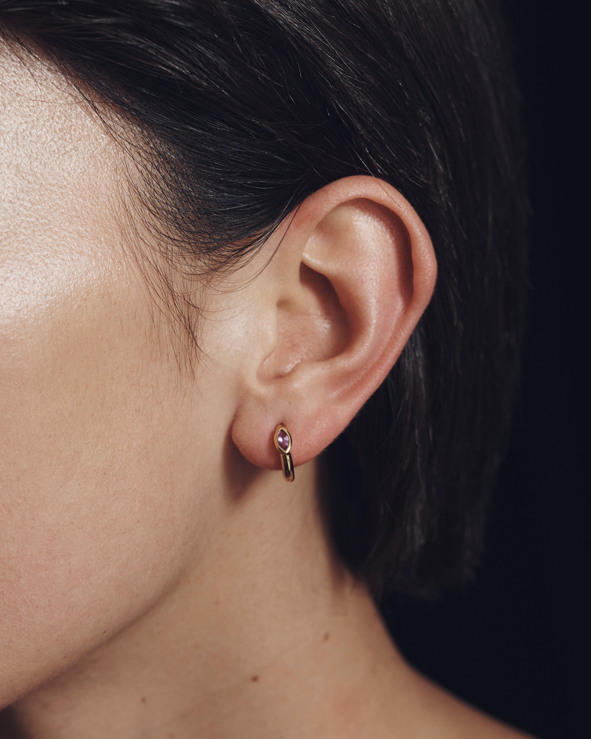 Close-up of an ear wearing a small earring with a dark background