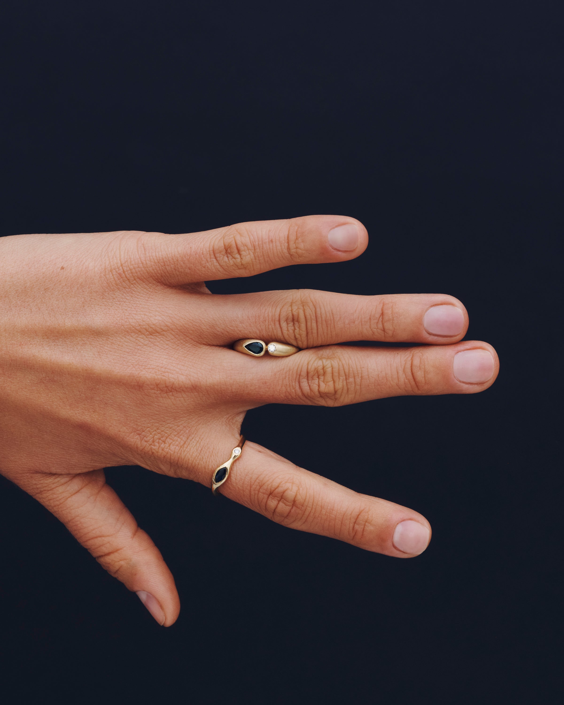 Hand wearing two gold rings with gemstones on a dark background