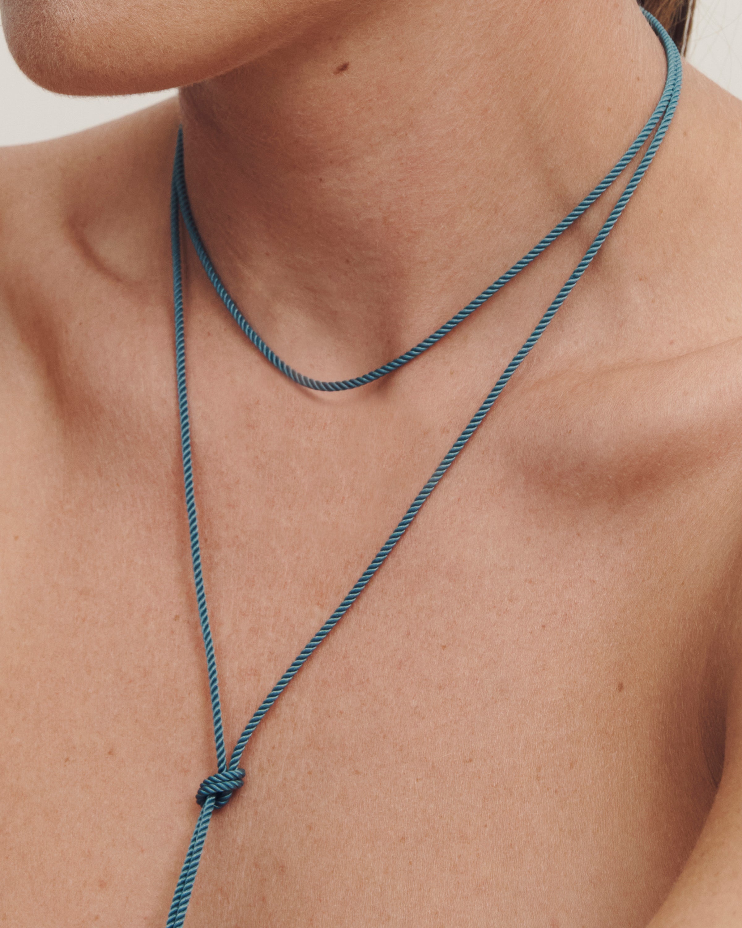 Close-up of a person wearing a blue necklace with a knot detail on a neutral background