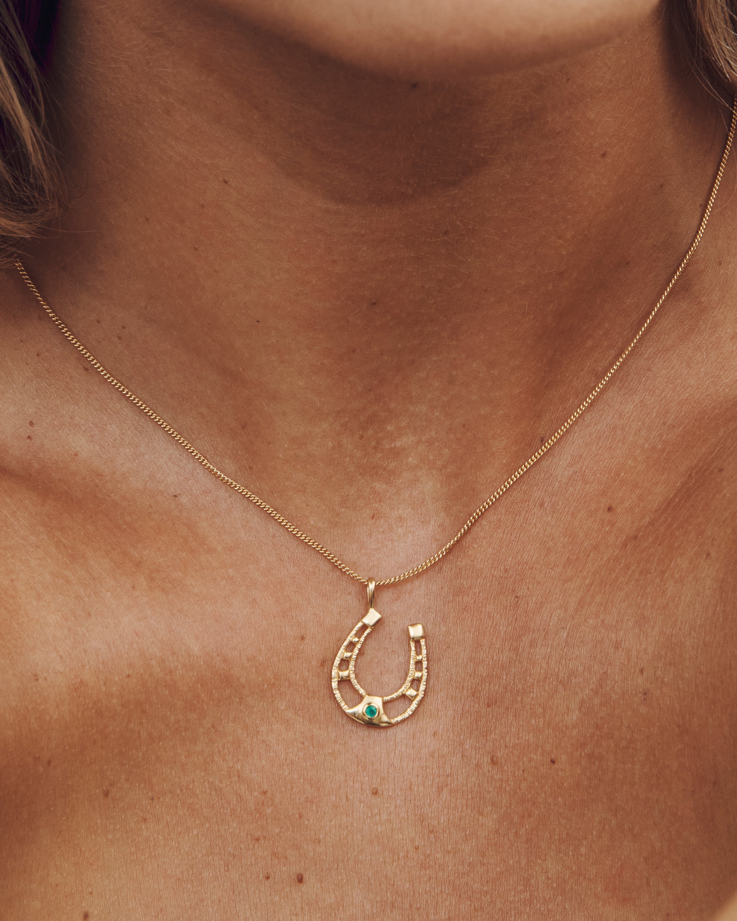 Gold necklace with a horseshoe pendant on a person's neck