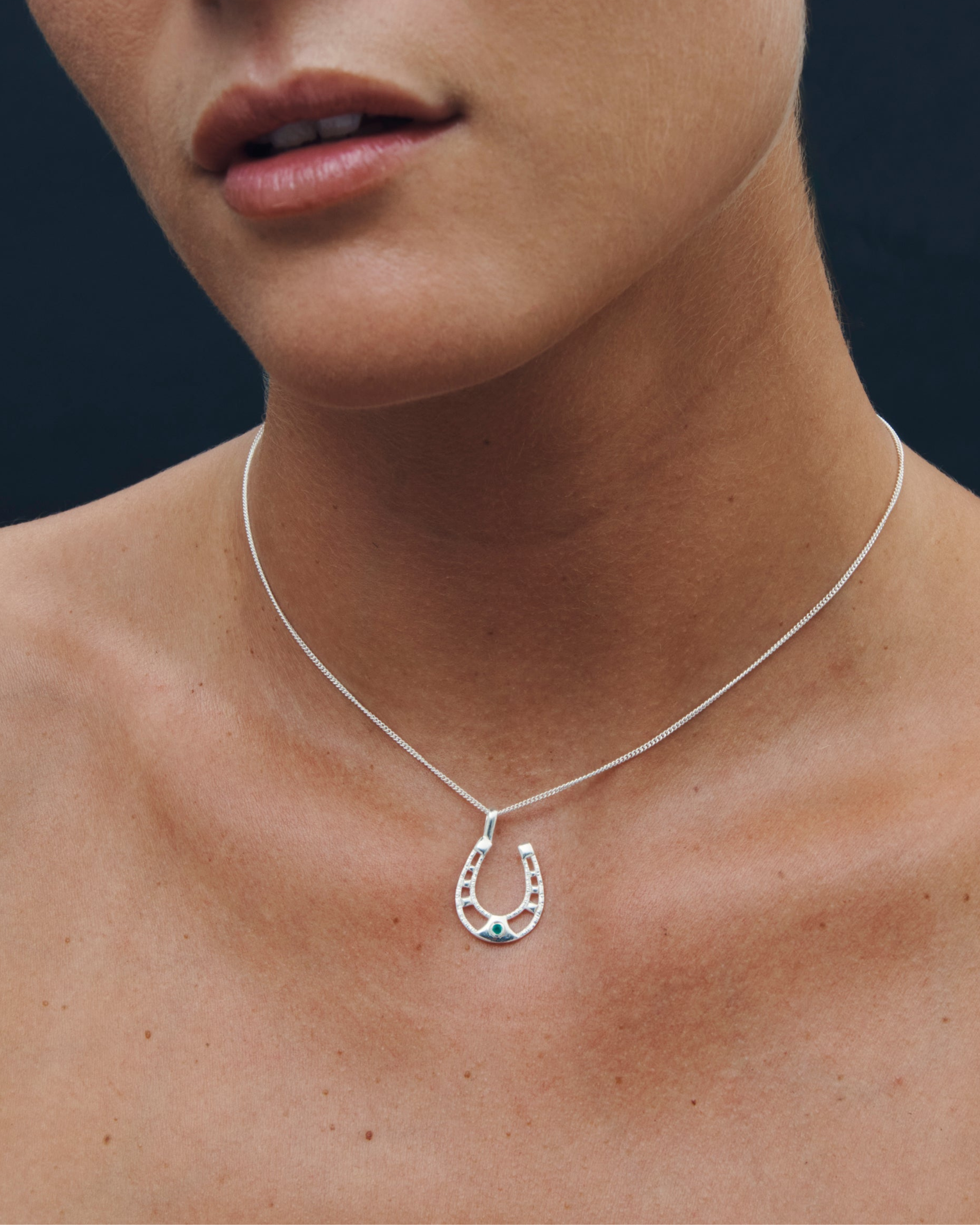 Close-up of a necklace with a horseshoe pendant on a person's neck against a dark background
