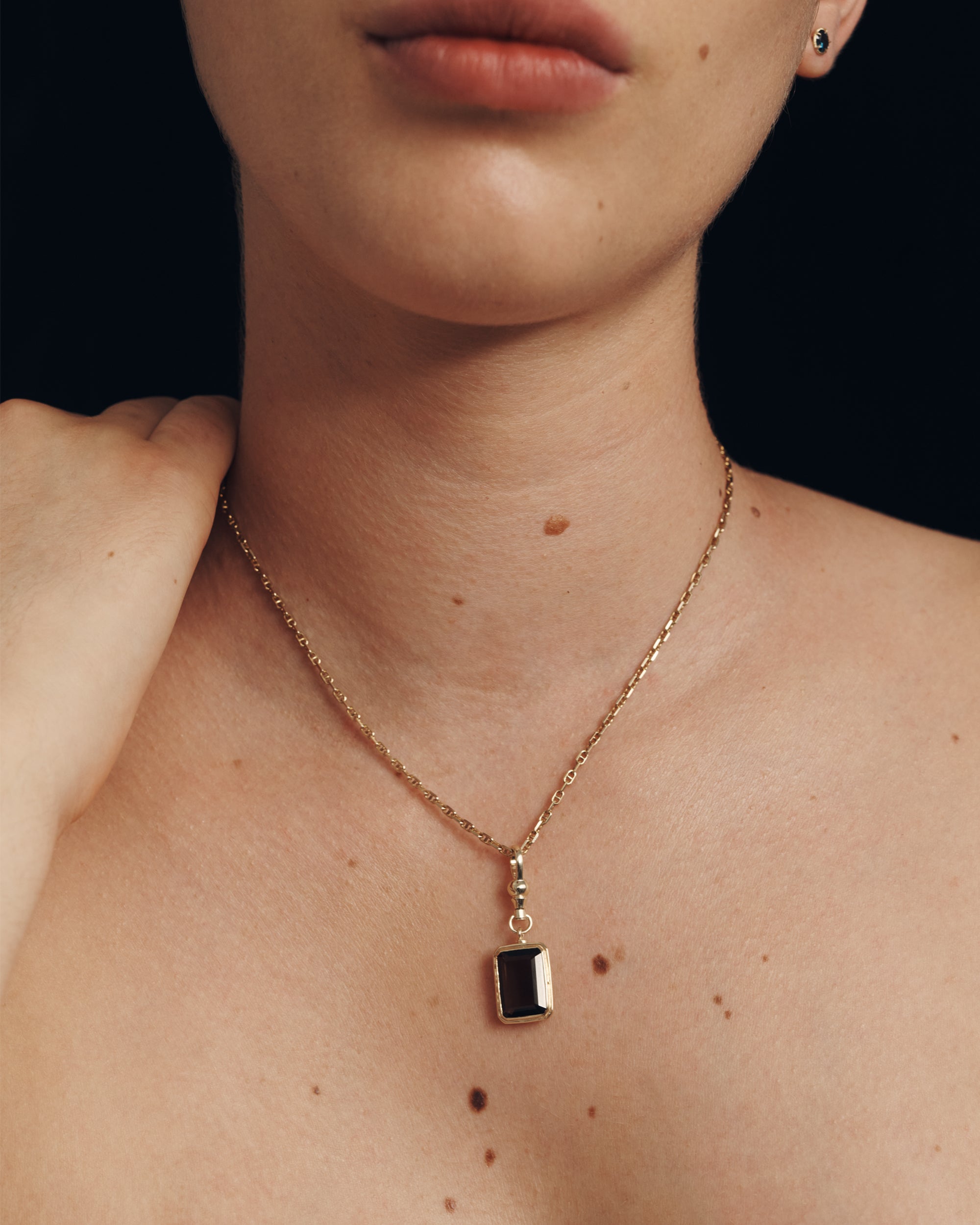 Necklace with a square pendant worn by a person against a dark background