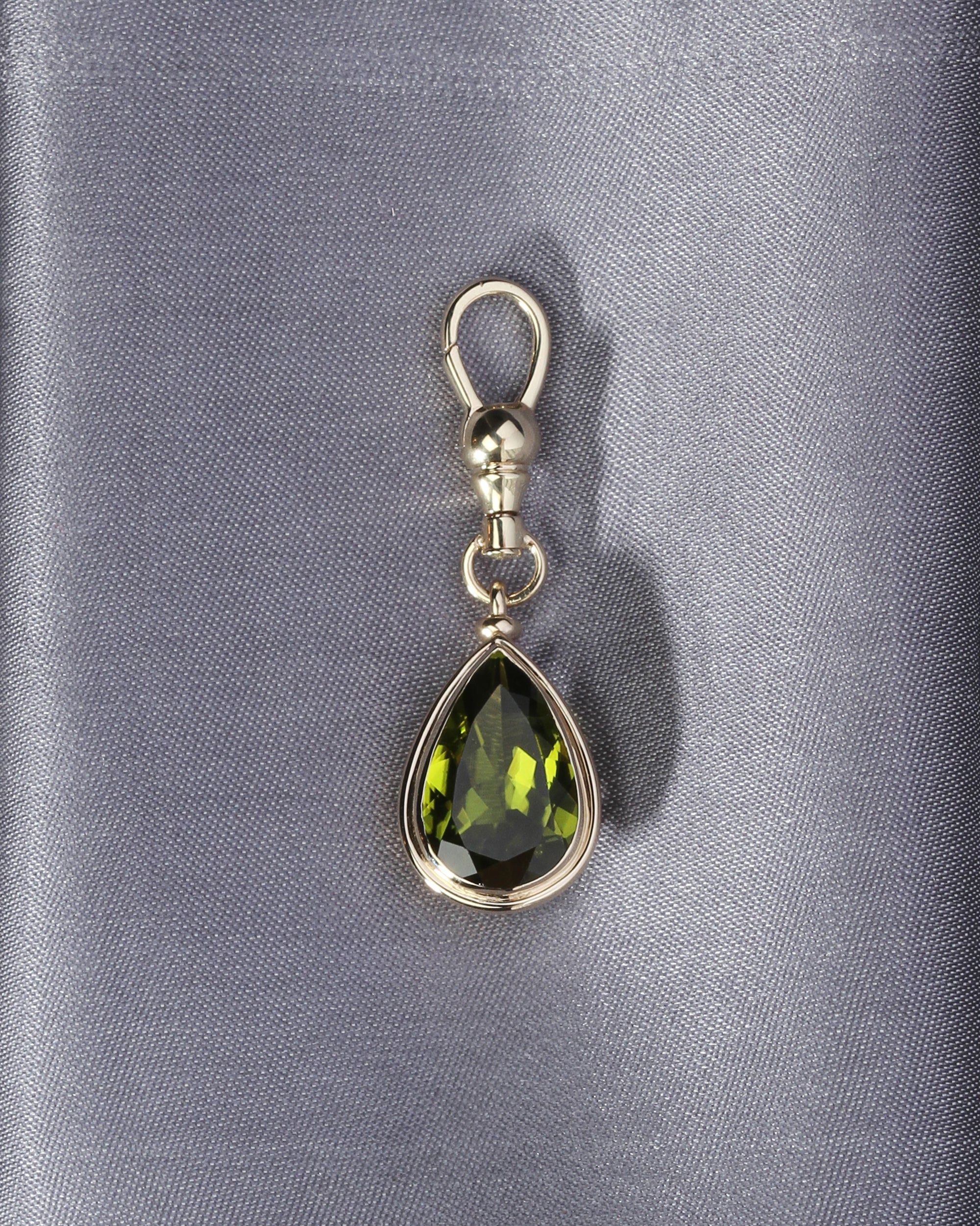 Teardrop-shaped green gemstone pendant on a silver chain against a gray background