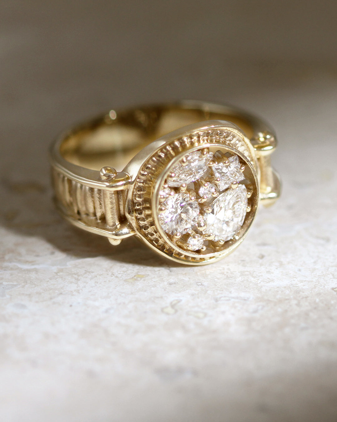 Pictured is a closeup of the Asteria Ring, a unique engagement ring inspired by ancient signet-rings with a round shaped signet filled with pear, marquise, princess and round brilliant cut lab-grown diamonds. Featuring a channel band with inset detailing and a high polish finish in solid yellow gold. 