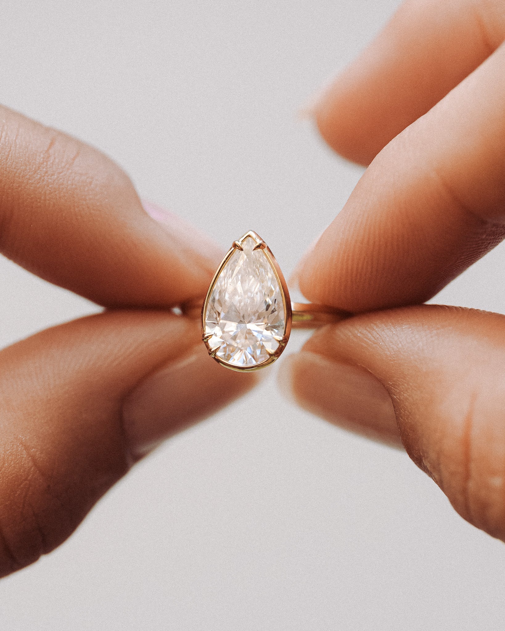 Teardrop-shaped diamond ring held between fingers against a neutral background