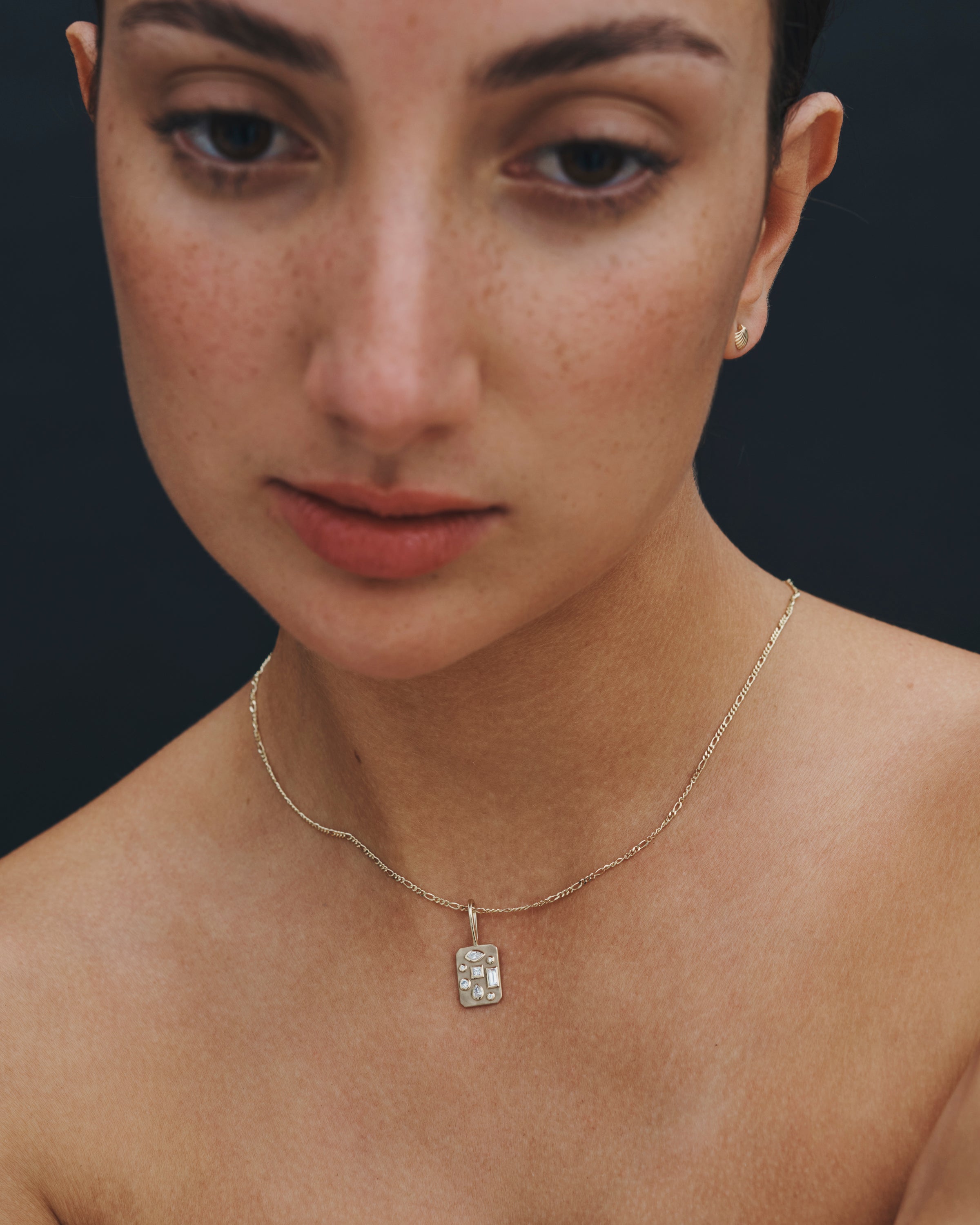 Close-up of a woman wearing a gold necklace with a diamond pendant against a dark background