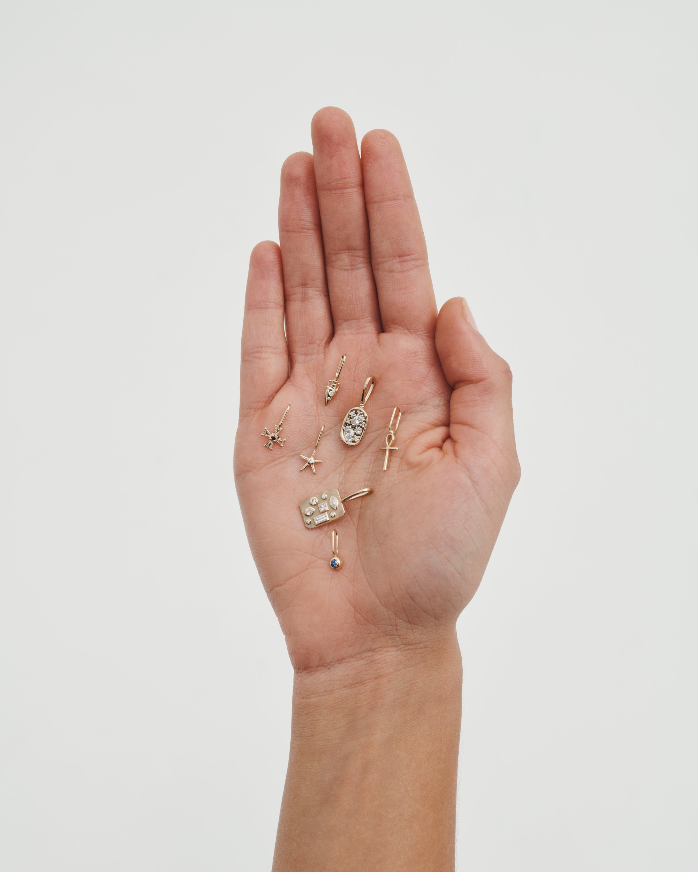 Hand holding various small jewelry pieces against a plain background
