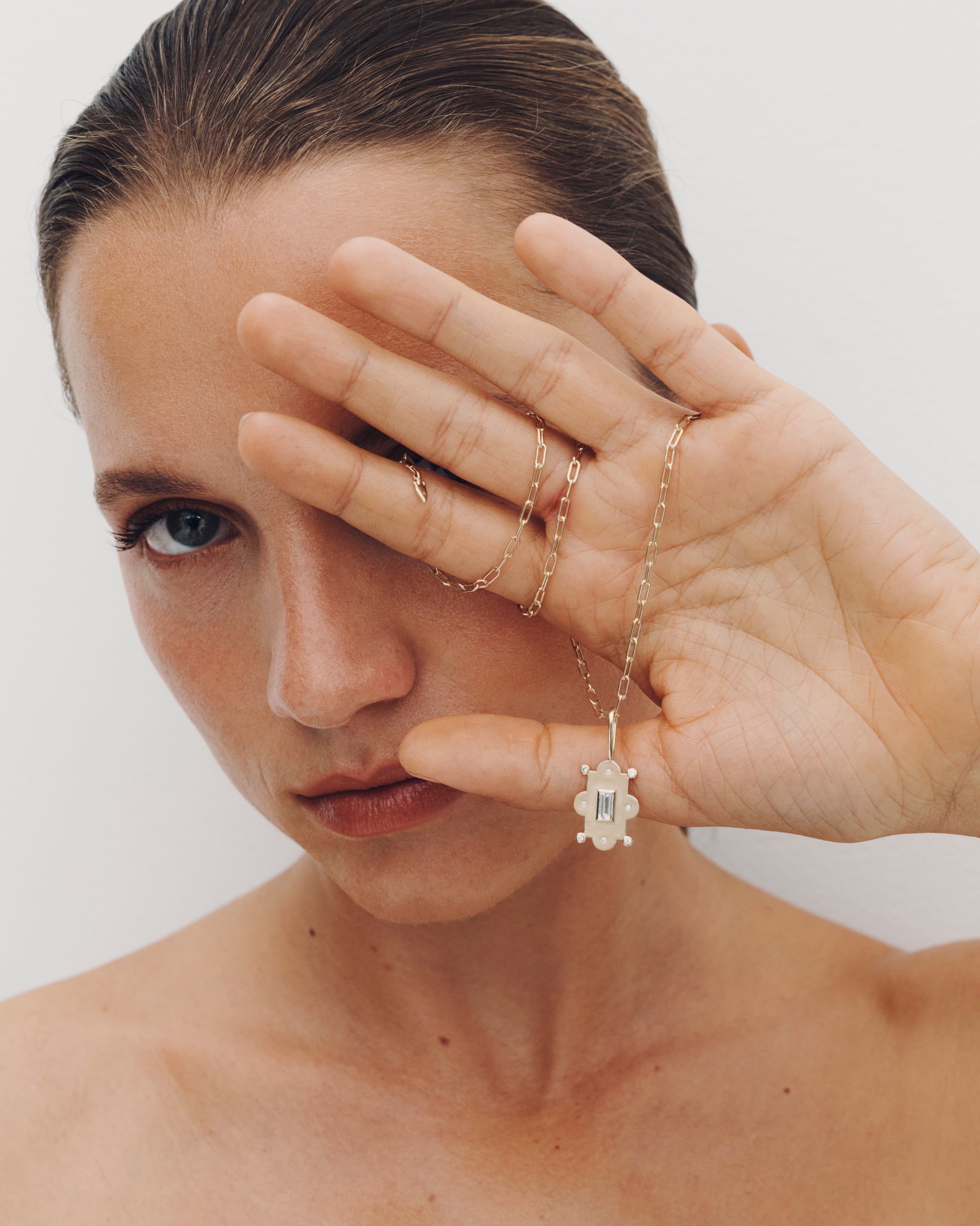 Woman wearing gold necklaces and rings, holding a necklace in front of her face.