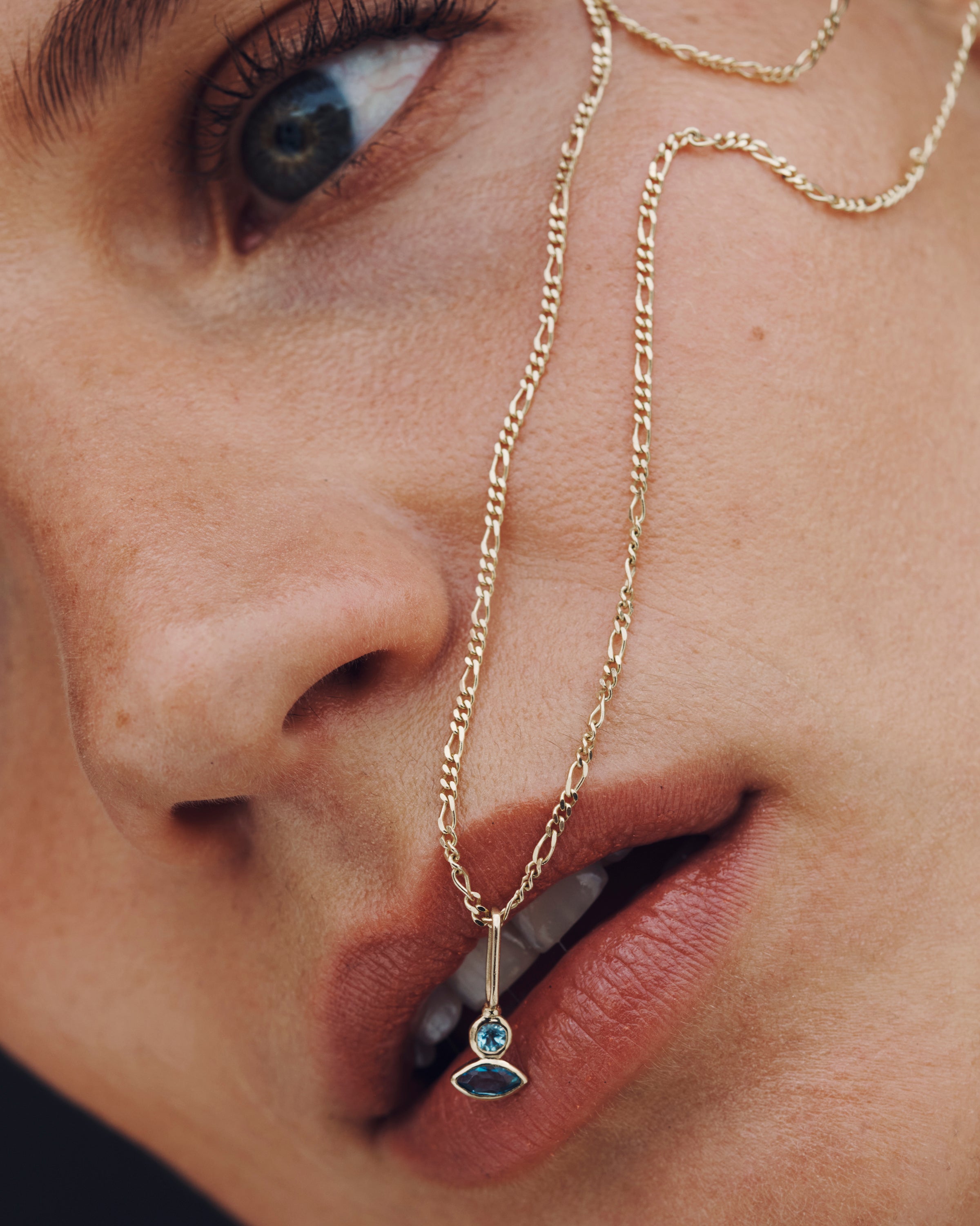 Close-up of a person wearing a gold necklace with a blue gemstone pendant.