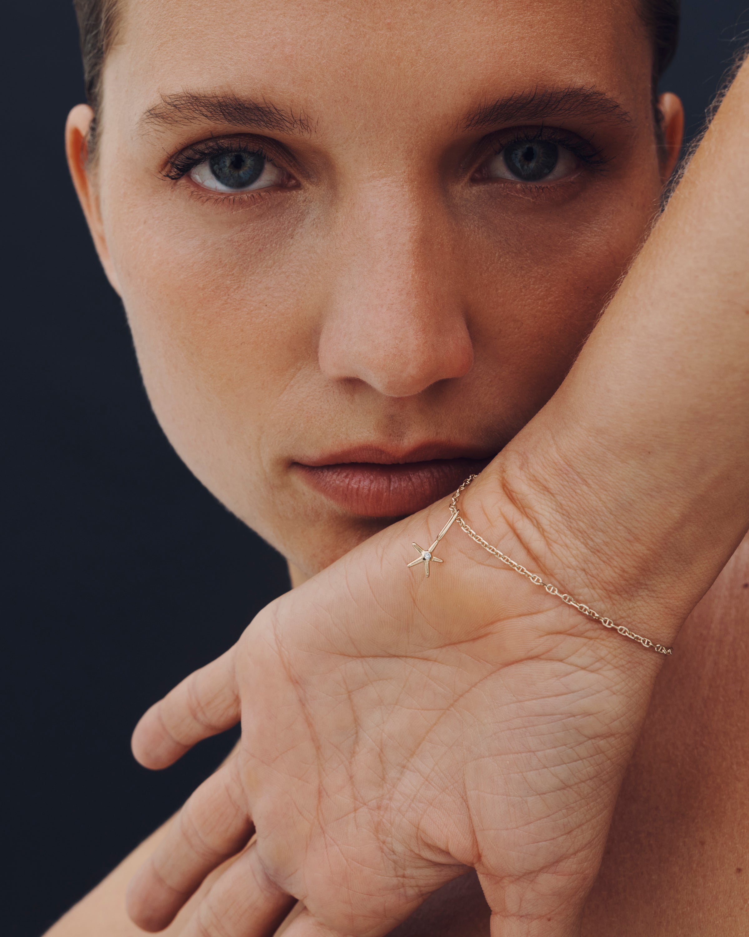 Close-up of a person wearing a delicate gold bracelet with a dark background