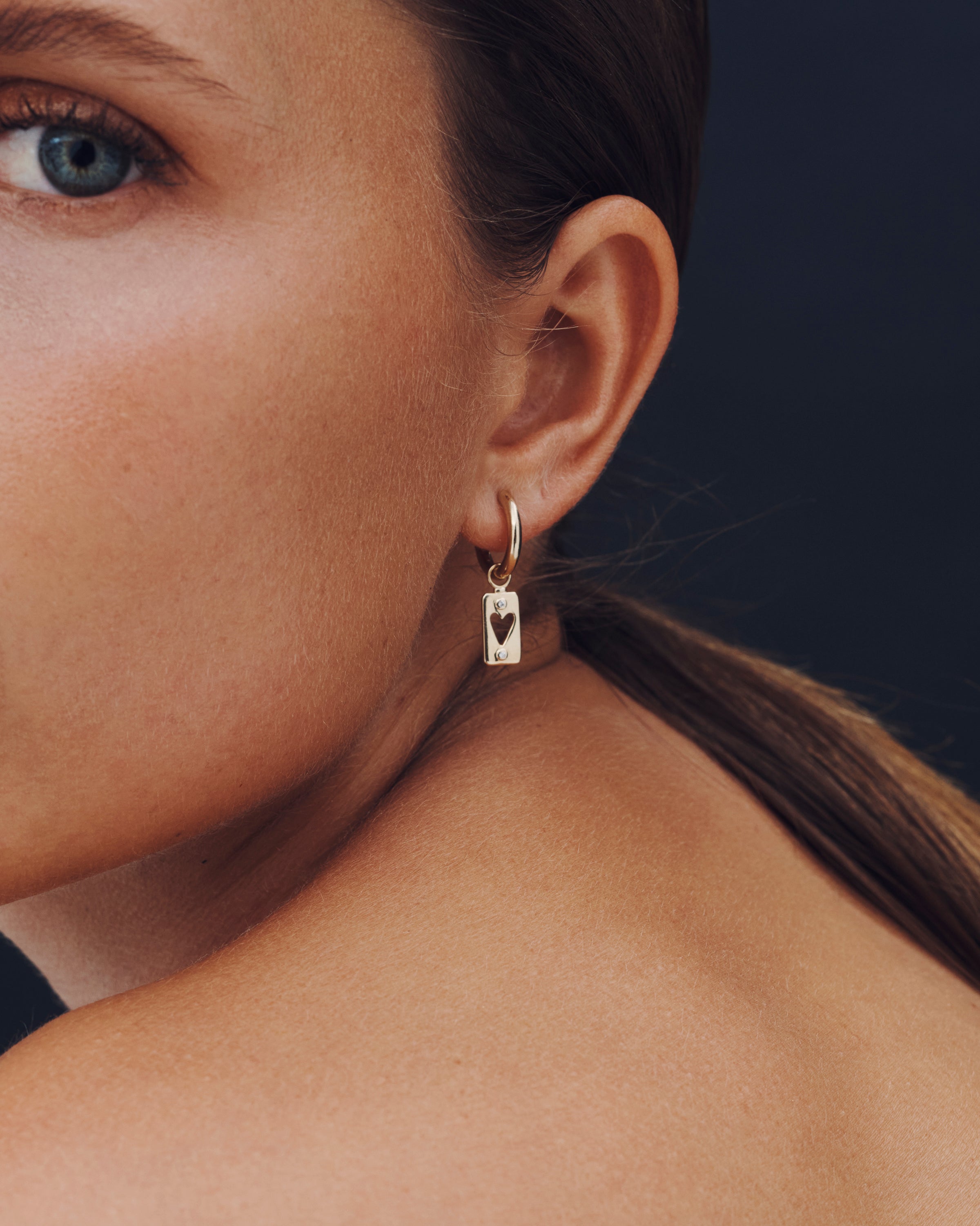 Close-up of a woman wearing a gold hoop earring with a heart pendant against a dark background