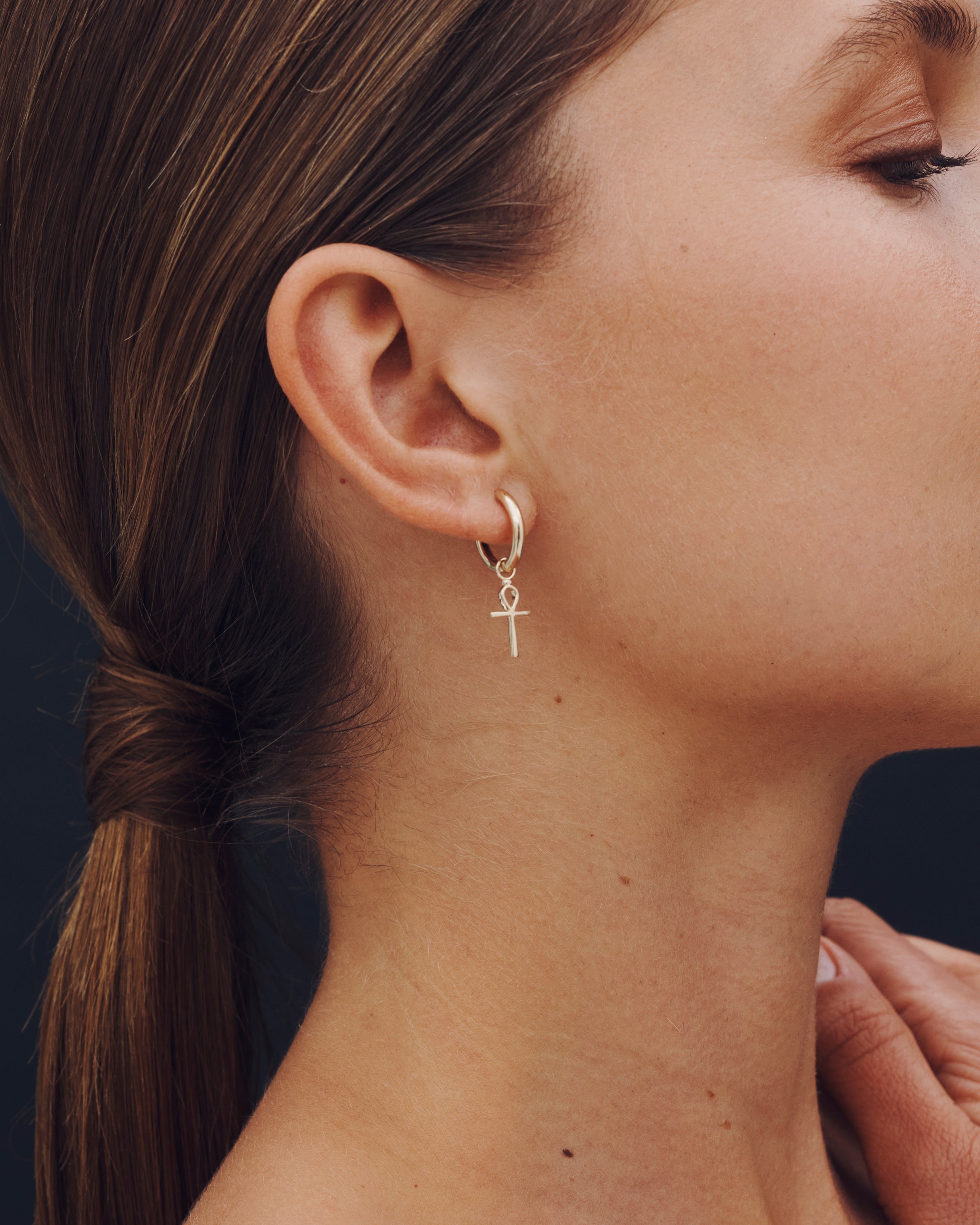 Close-up of a woman wearing a gold cross earring against a dark background