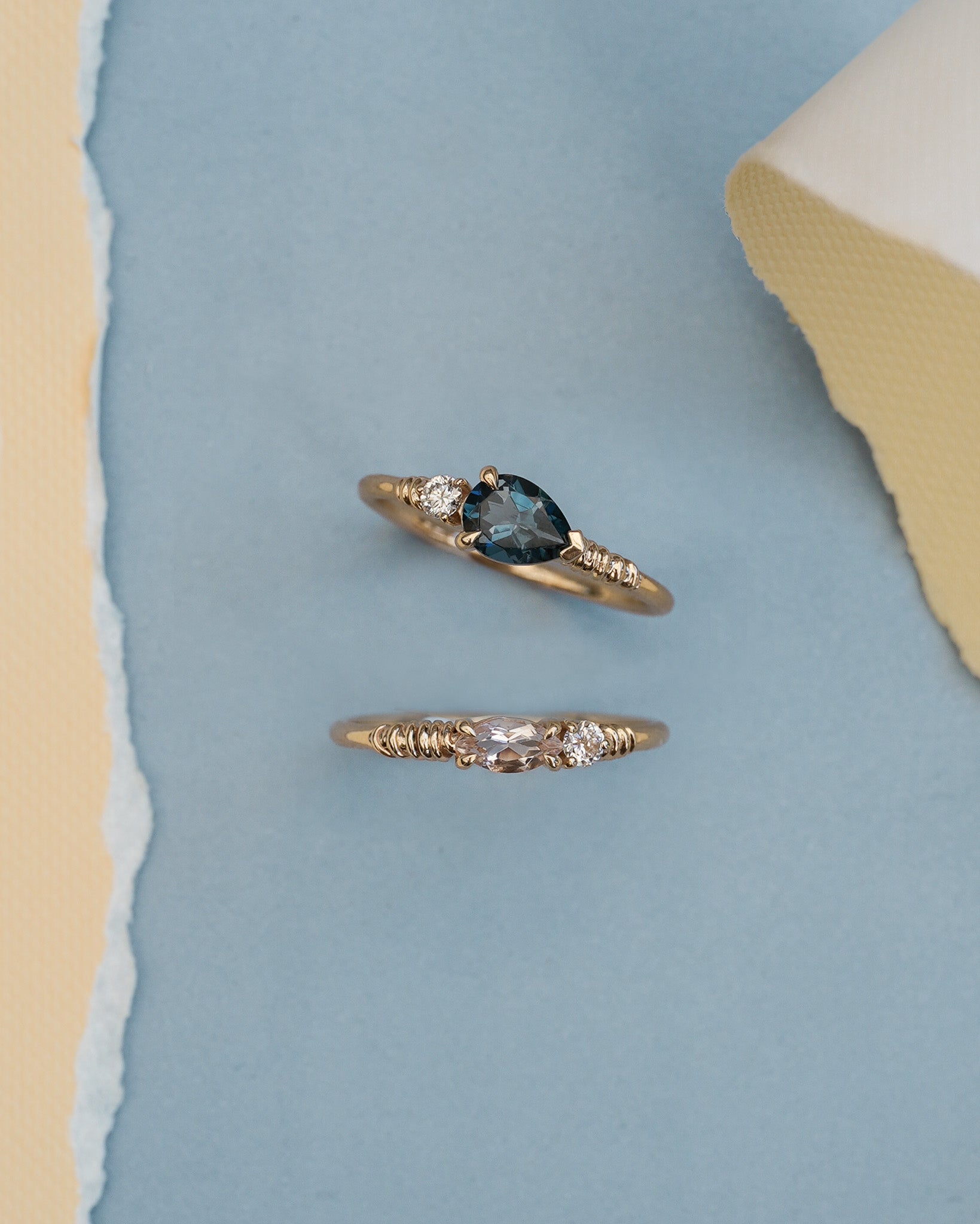 Two gold rings with gemstones on a light blue and beige background