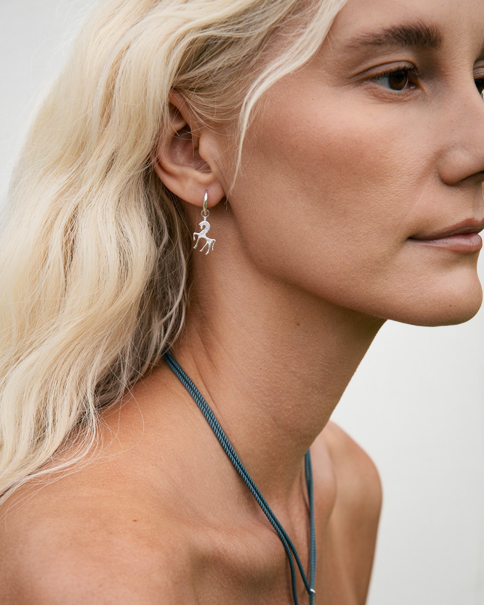 Close-up of a woman wearing silver unicorn earrings with a neutral background