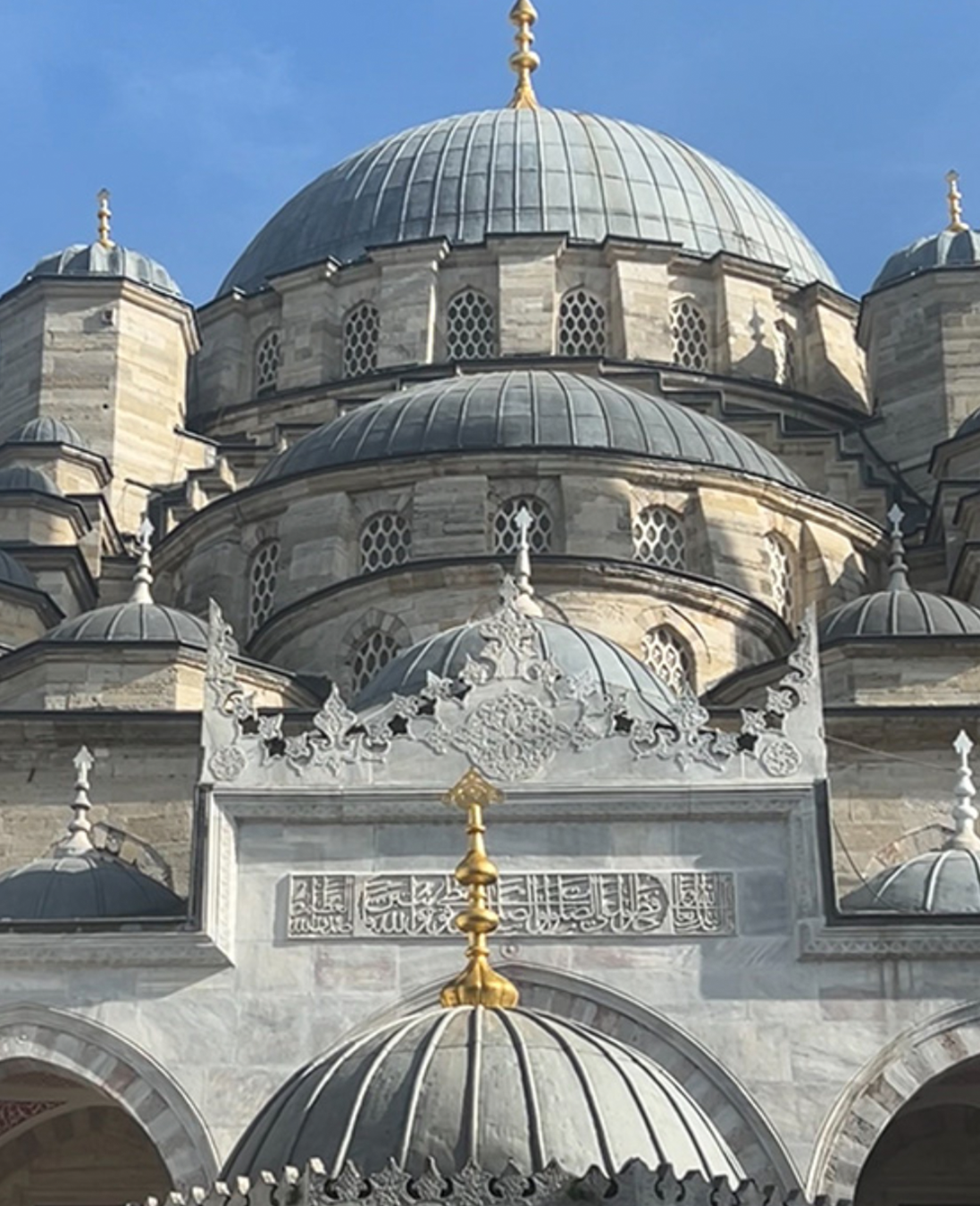 Close-up of a mosque with domes and intricate architecture against a blue sky.