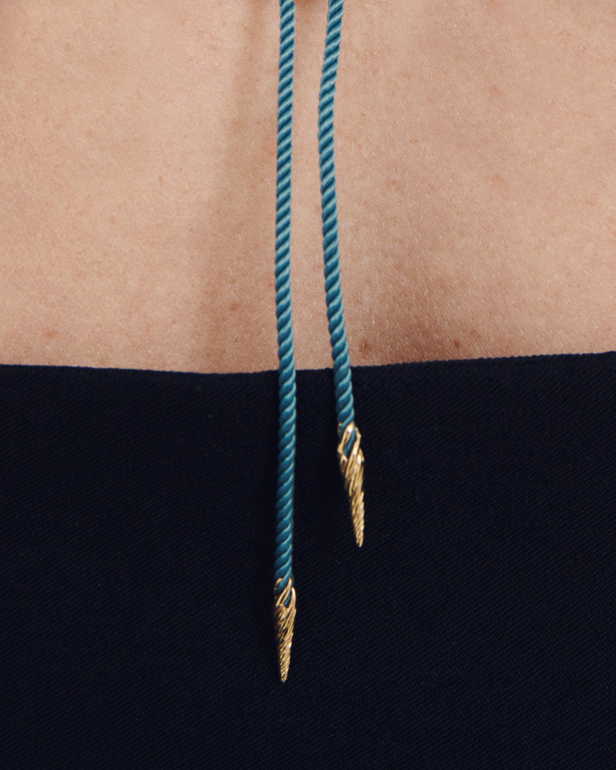 Blue rope with gold ends hanging from a person's waist against a black background