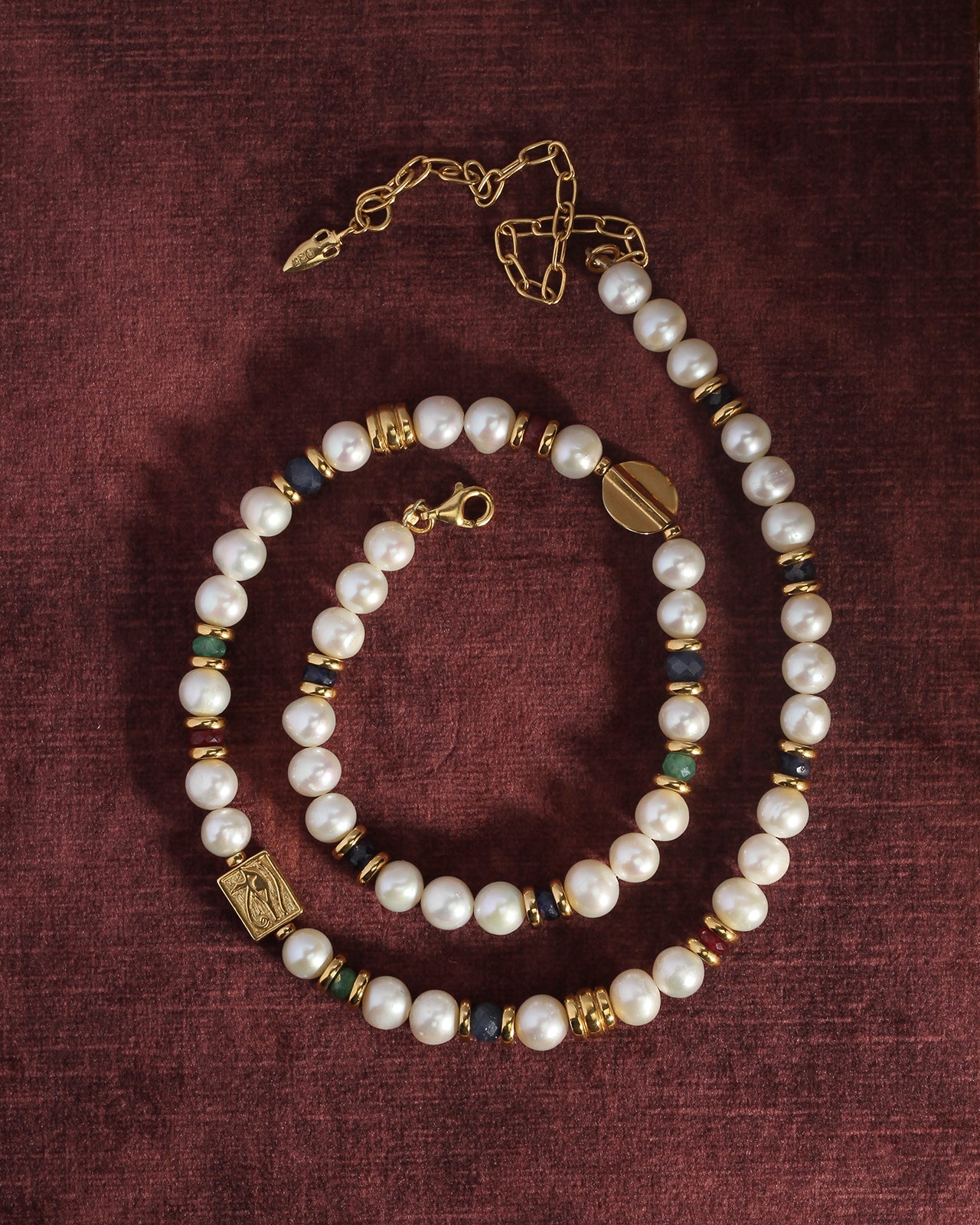 Pearl necklace with gold and blue accents on a maroon fabric background