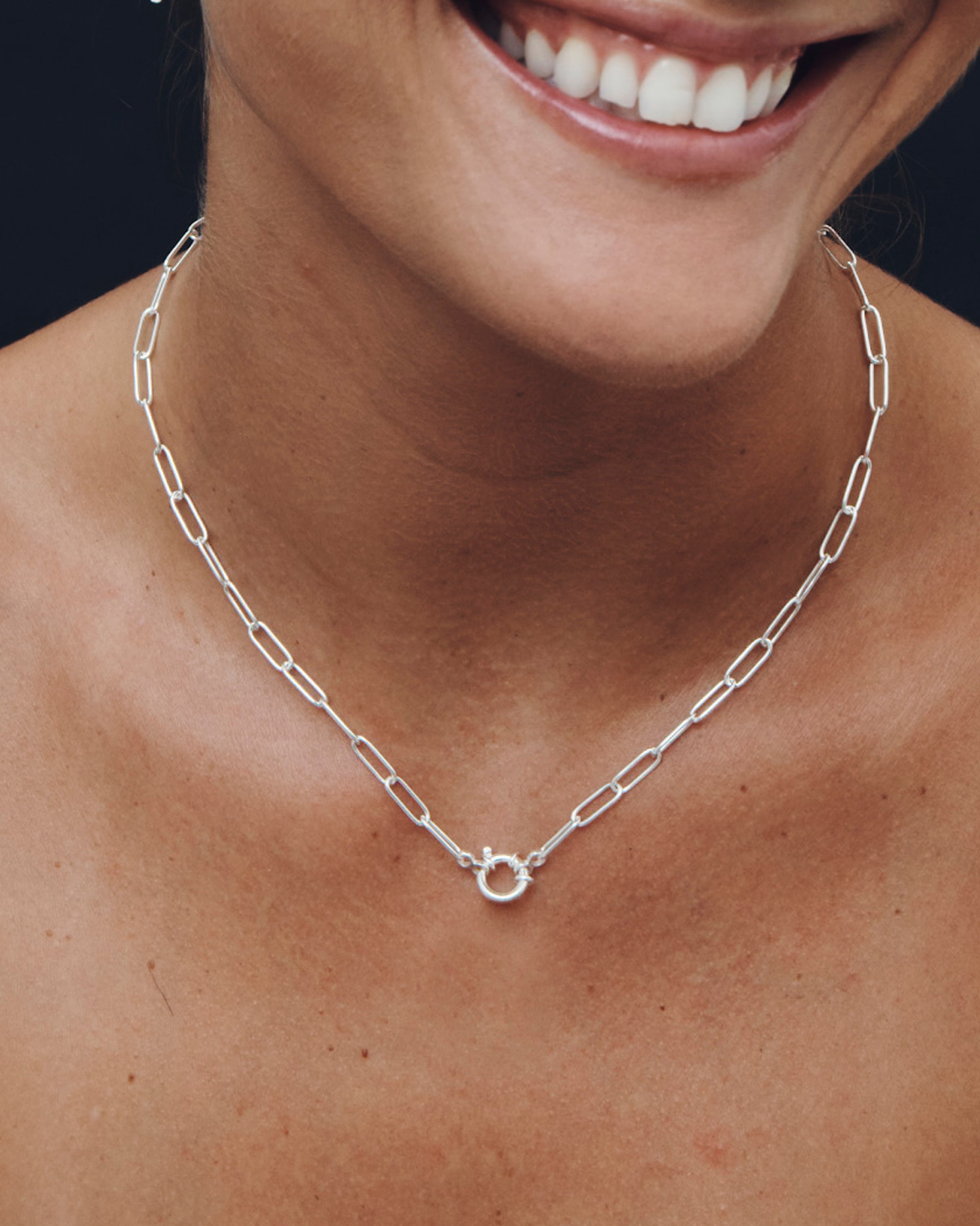 Silver chain necklace worn by a person with a dark background
